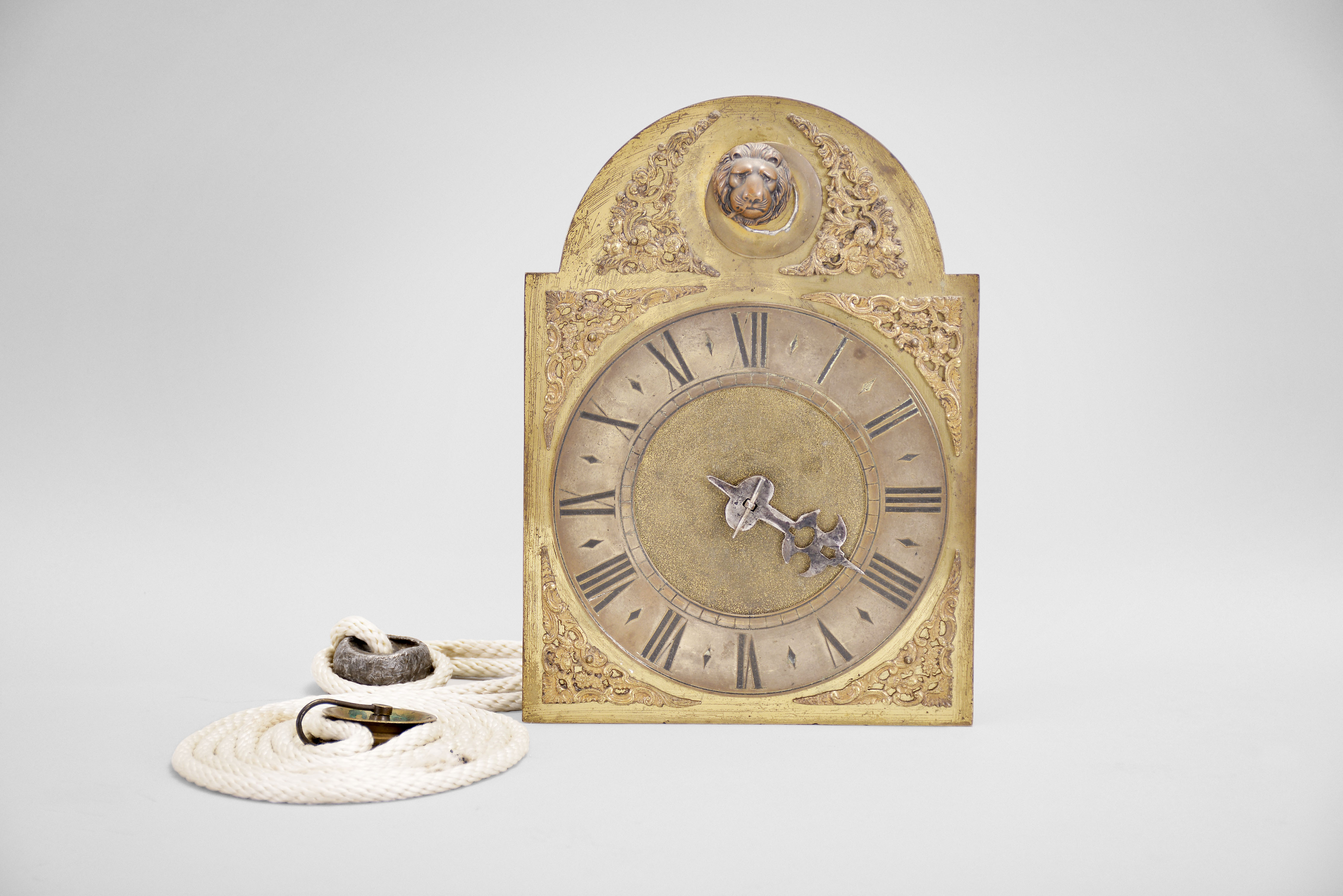 England, a mid 18th century, 30 hour posted frame clock with bracket, arched brass composite dial with matted center, roman numeral silvered chapter ring, single cut steel hand, iron movement with rectangular posts, seconds pendulum, and count wheel striking, brass clad weight, and 20th century bracket. — Antique Clocks Price Guide