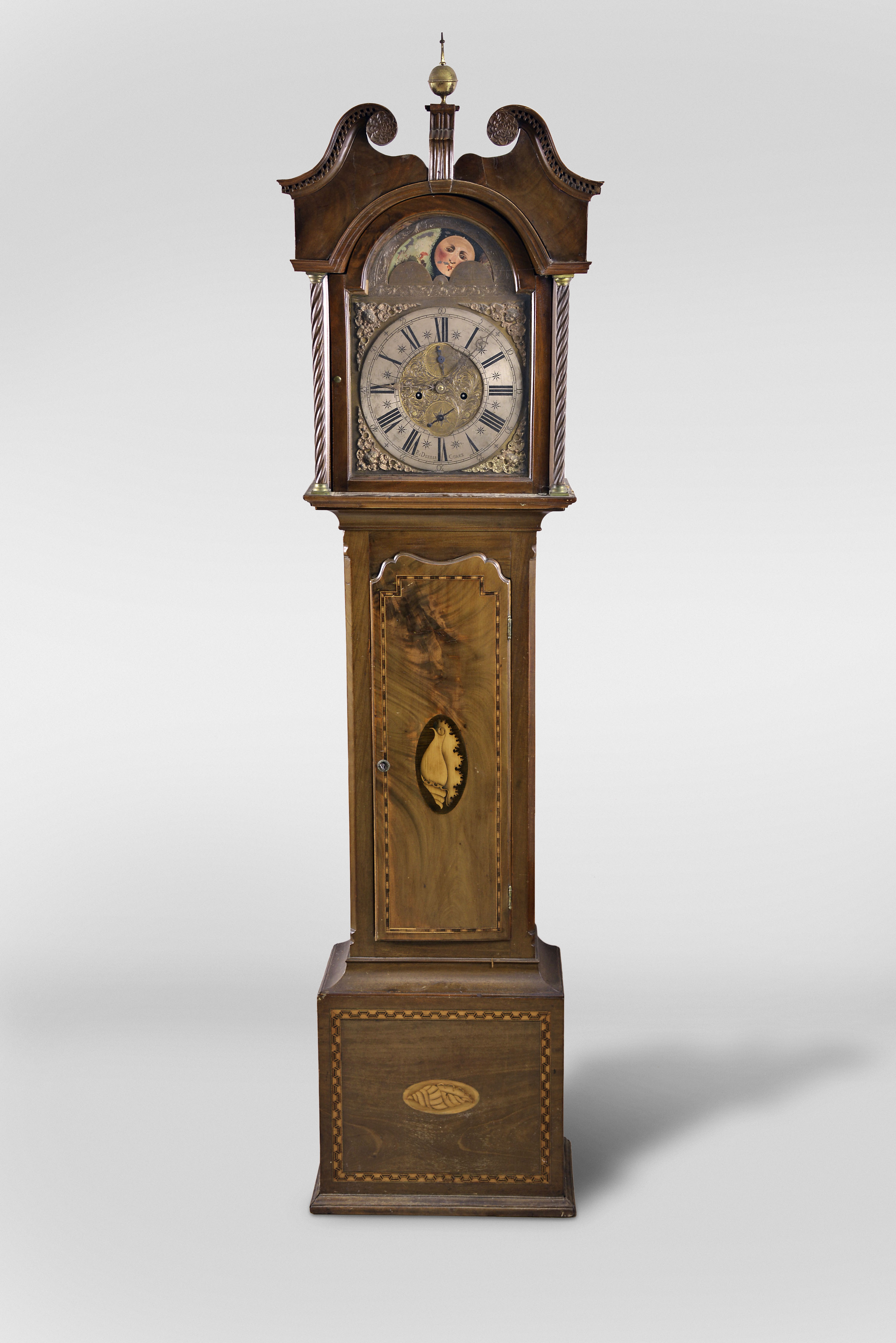 Ri. Deeble, Cork, Ireland, tall clock, 8 day, time and strike, weight driven movement in an inlaid mahogany case with broken arch top, dentil molding, carved rosettes and rope twist columns flanking hood over inlaid trunk door and base. The brass dial has calendar, silvered chapter ring, cast corner spandrels and moon phase. — Antique Clocks Price Guide