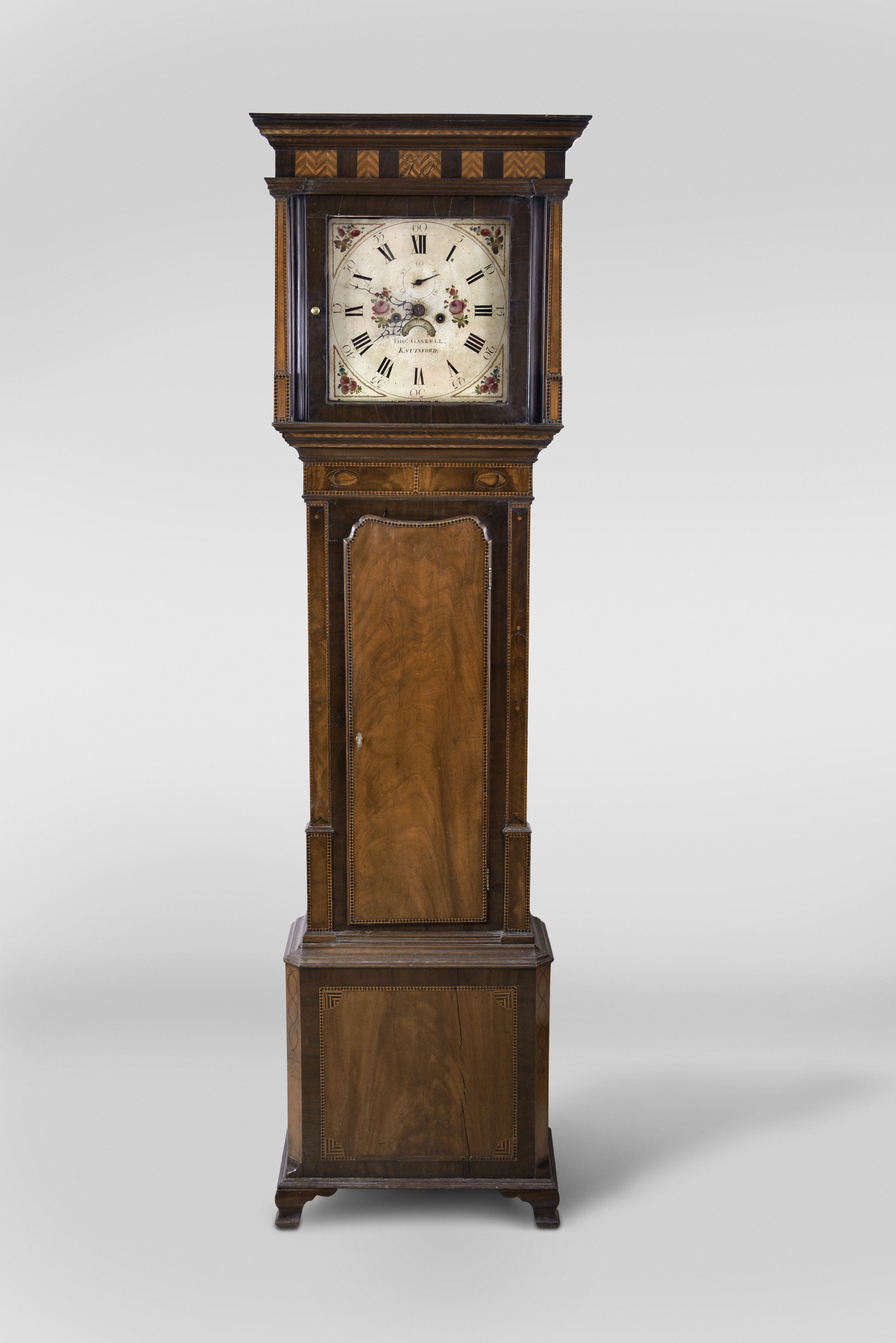 Thomas Gaskell, Knutsford, County Cheshire, England, tall clock, 8 day, time and strike, weight driven movement in a flat top heavily inlaid mahogany case with cross hatching and conch shell decorations. The painted metal square dial has seconds bit and calendar. — Antique Clocks Price Guide