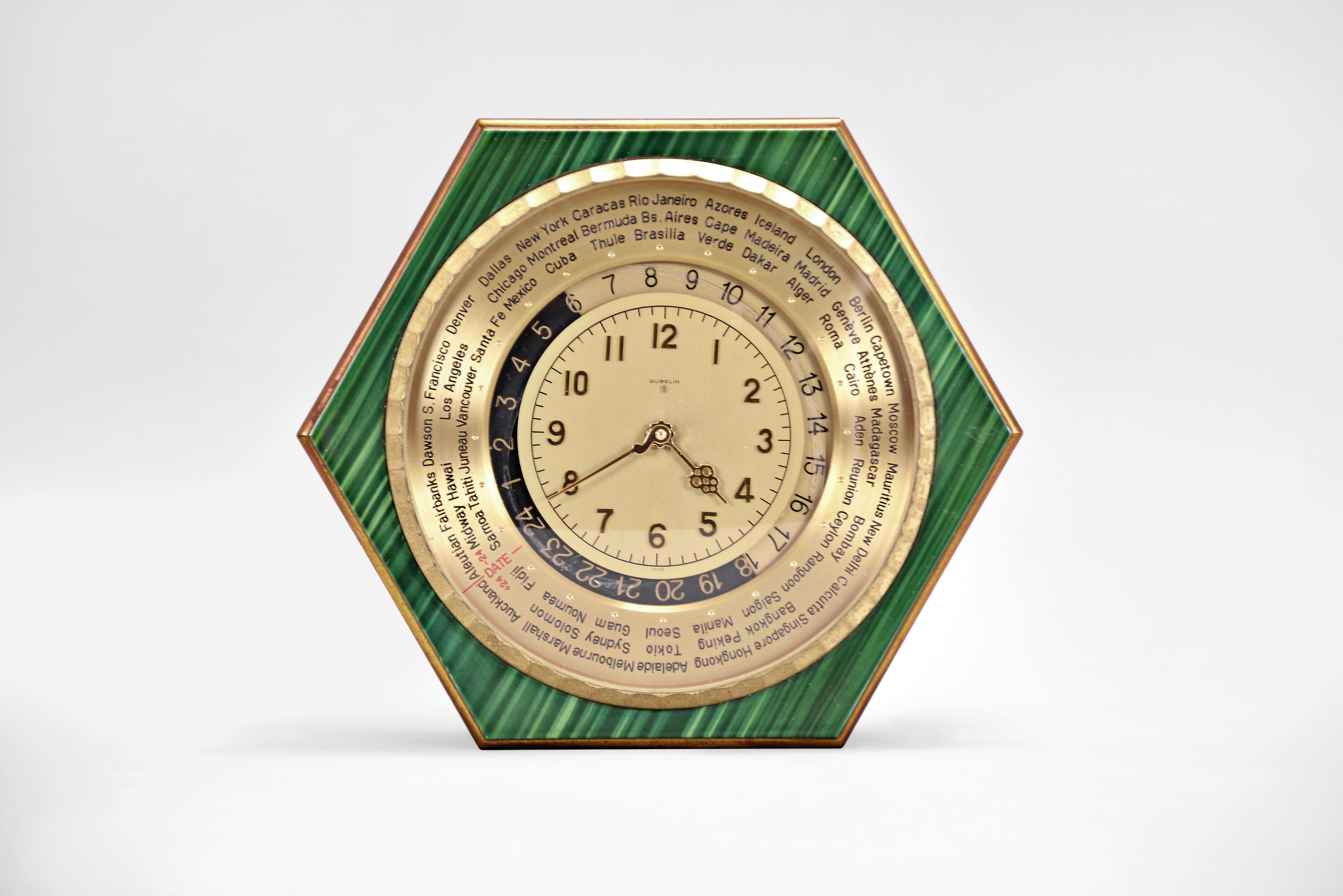 Gubelin, Switzerland, a hexagonal, faux malachite and gilt brass world time table clock, the case on compressed ball feet with upper and lower plates connected by pillars, and separated by a cylindrical mid section, fluted bezel with convex glass, the time display with outer ring engraved with important international cities, surrounding a 24 hour dial, and with central 12 hour dial, powered 8 day timepiece movement with lever escapement — Antique Clocks Price Guide
