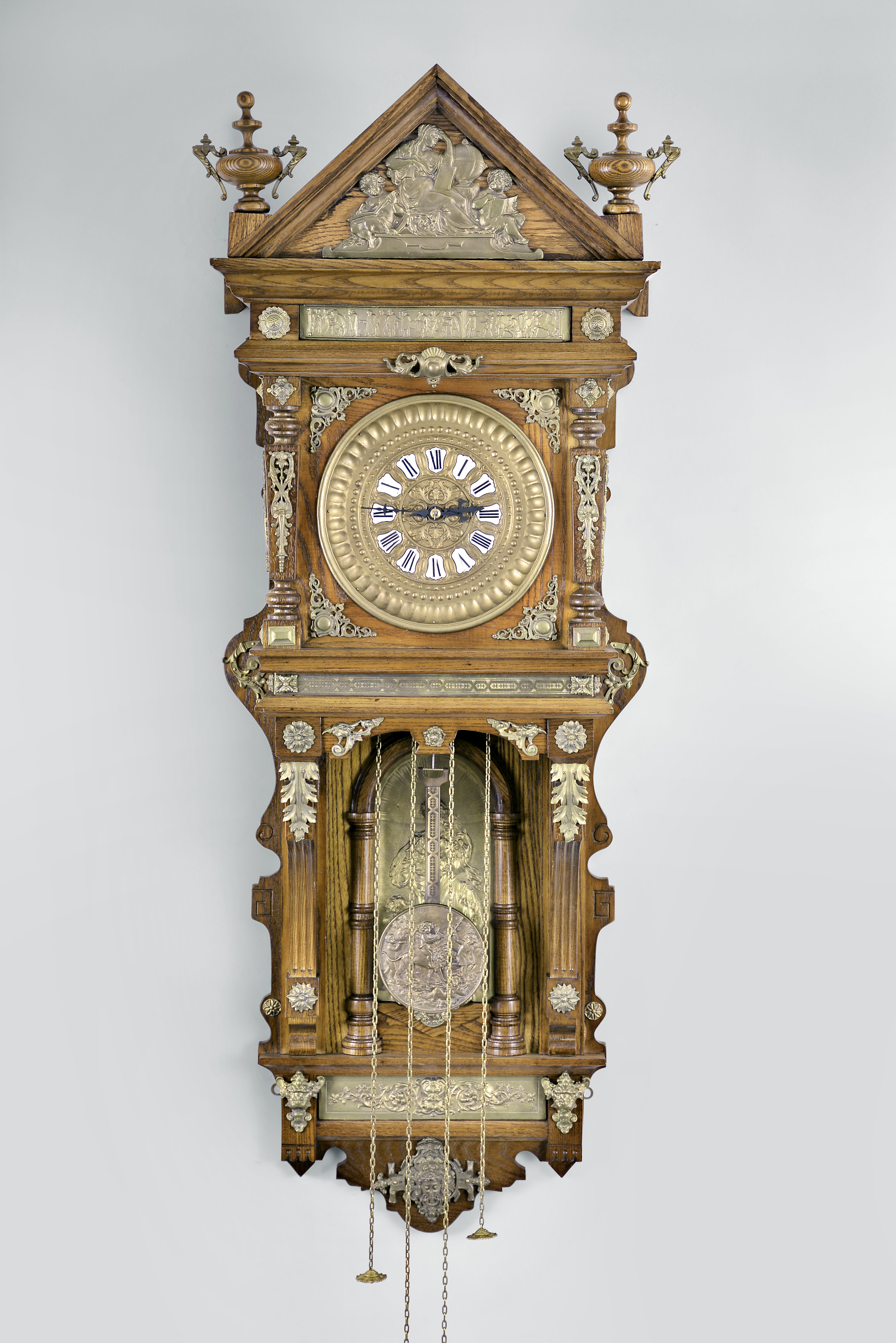 Reproduction Ansonia, "Hanging Antique", 8 day, time and strike, weight driven movement in an oak case with applied brass ornaments, brass dial with enamel cartouche numerals, and blackened steel hands. — Antique Clocks Price Guide