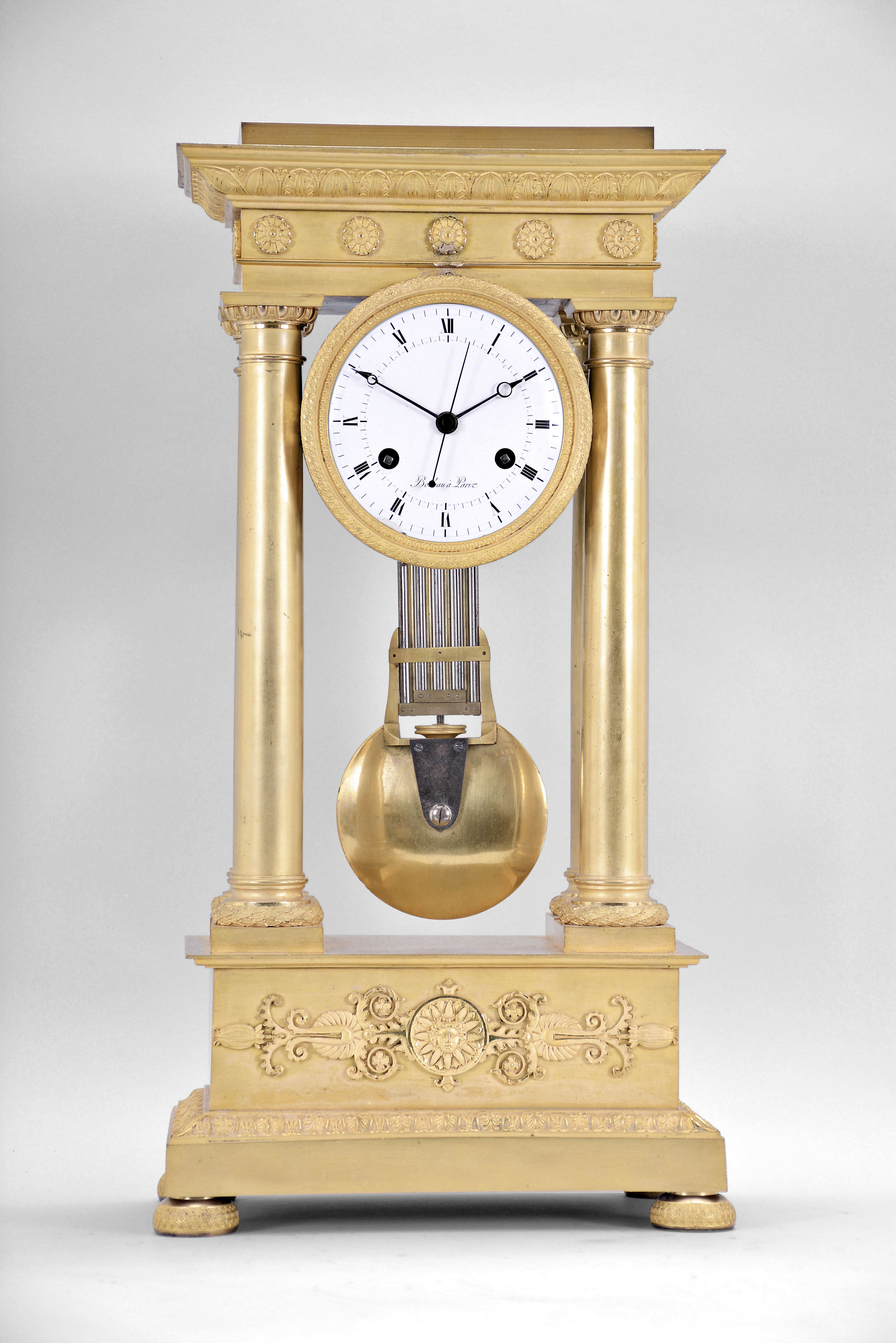 Boileau a Paris, an early 19th century, half seconds beating gilt bronze portico clock, on floral medallion ornamented compressed ball feet, base molding decorated with palmette, anthemion and bellflower, the dado with mount having a central sunflower with mask, and flanking Grecian foliate ornament below the simple molded surbase, four columns with square plinths, laurel wreathed molded bases, and egg and dart capitals supporting the entablature, the frieze with floral medallions and cornice with waterleaf, palmette and bellflower, laurel wreath bezel with simple foliate inner ring, roman numeral white enamel dial with inner seconds chapter,signed "Boileau a Paris", blued steel Breguet style hands and central seconds hand, large two train movement with knife edge suspension and pin wheel escapement, counting the hours on a bell, and heavy bimetallic half seconds beating gridiron pendulum — Antique Clocks Price Guide