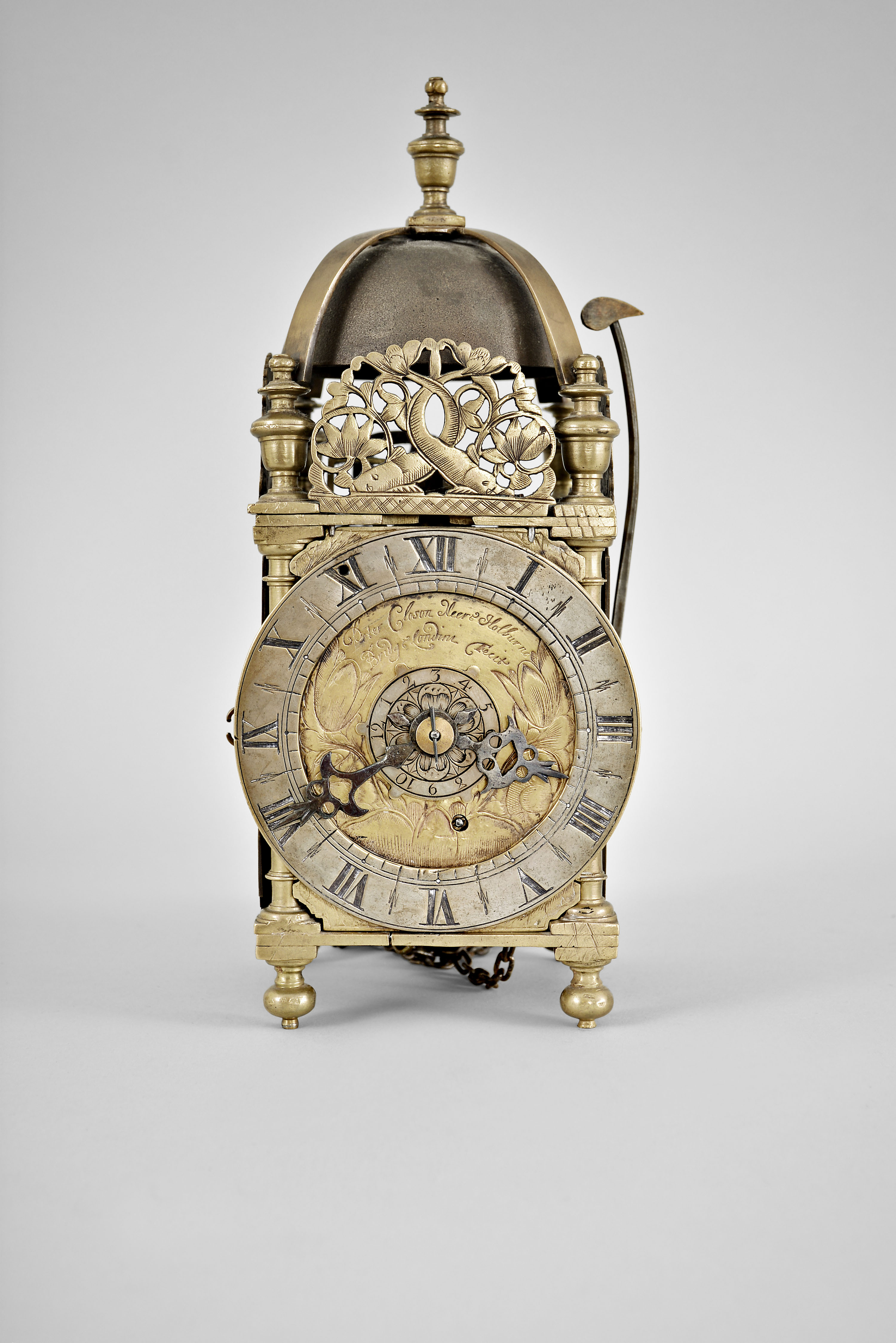Peter Closon, London, a mid 17th century miniature striking lantern clock, the brass case with turned, tapered columns at the corners, with ball feet and urn finials, three sides with engraved, dolphin frets, and top with brass bell strap with finial and bell, dial plate with engraved tulips, and signed "Peter Closon Neere Holburn Bridge Londini Fecit", silvered brass chapter ring with roman numerals and matchstick flower half hour markers and blued steel hands, movement with crown wheel escapement and count wheel striking, contrate and crown wheels without crossings, with 20th century wall bracket — Antique Clocks Price Guide