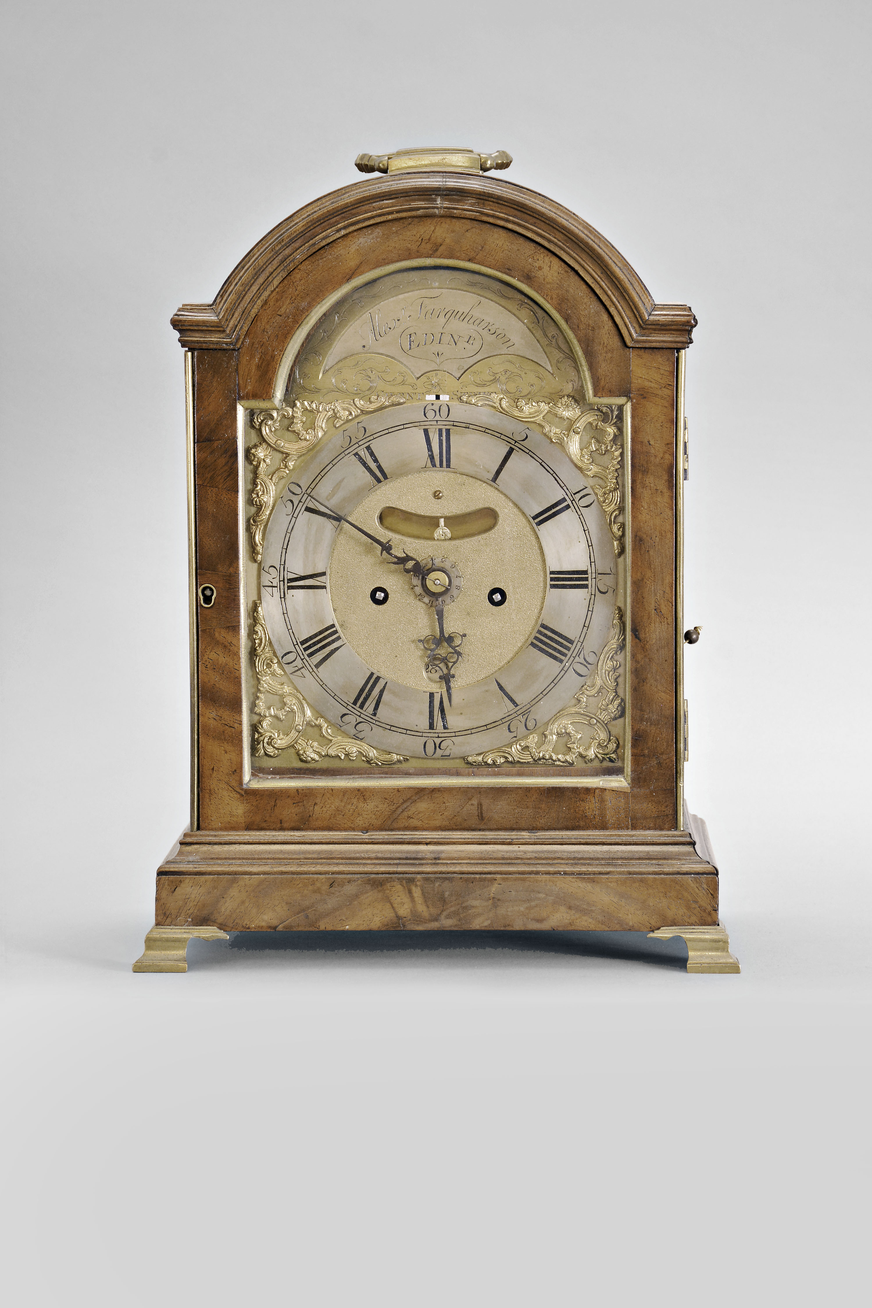 Alexander Farquharson, Edinburgh, Scotland, a mid 18th century mahogany bracket clock with date and alarm, molded base on brass bracket feet, door with brass beads at sides, and brass molded light, break arch molded top with carrying handle, the sides with brass fishscale fretsbrass composite dial with silvered, roman numeral chapter ring, matted center with date aperture above 6:00, and cutour to view mock pendulum below 12:00, and arch with silvered brass panel engraved with the makers name and location, pierced blued steel hands, 8 day fusee movement with five pillars, engraved back plate, recoil escapement, and striking on a bell — Antique Clocks Price Guide