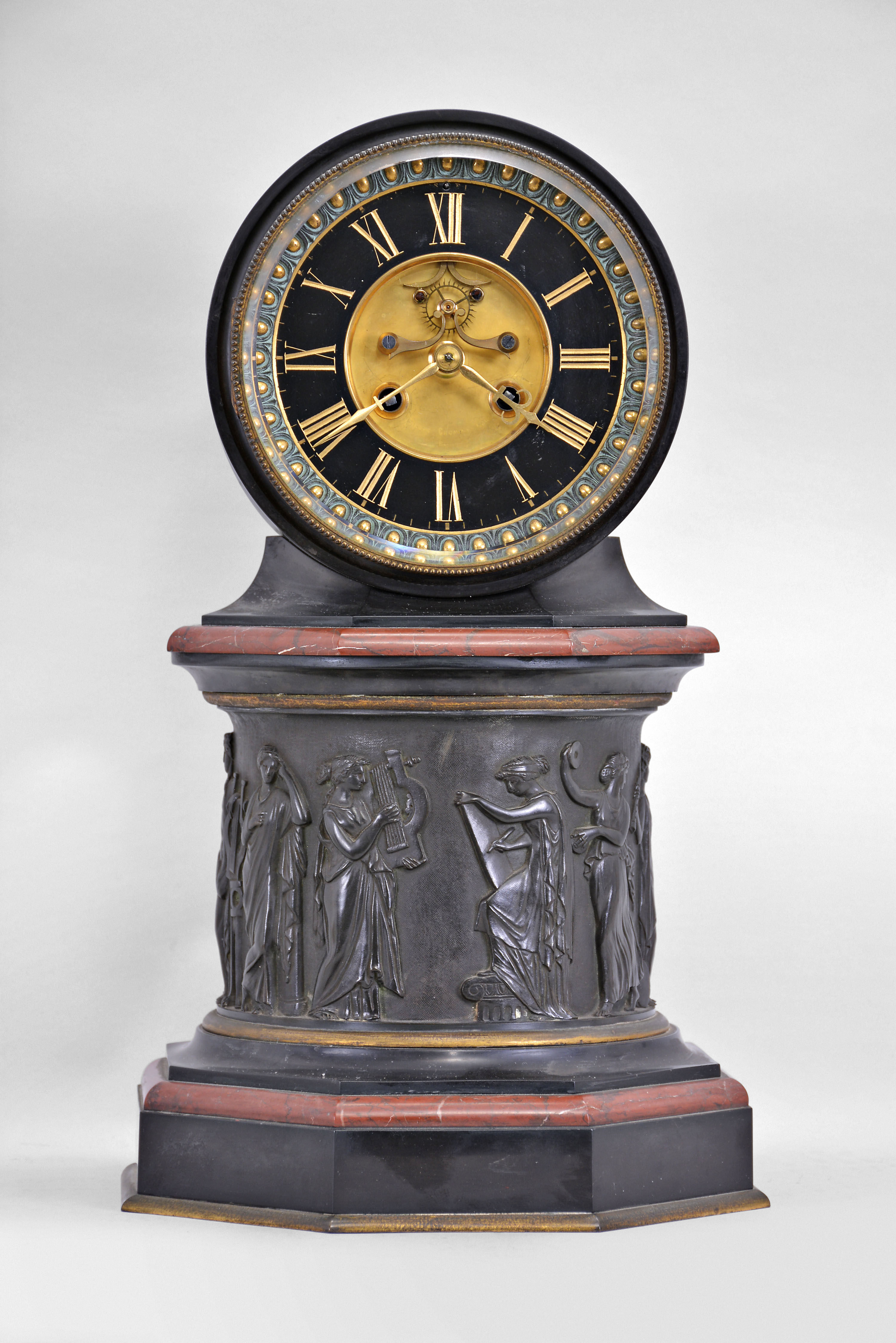 E. Maurice and Co., Paris, France, for Shreve, Crump & Low, Boston, mantel clock, 8 day, time and strike, spring driven pendule de Paris movement with visible Brocot escapement on an molded octagonal base with gilt brass and red marble ovolo molding supporting a central column with the Greek muses cast with relief from patinated metal, supporting a molded octagonal capital upon which rests a drum head of black slate holding the movement, bezel, and polished black slate dial with incised Roman numerals and gilt hands. — Antique Clocks Price Guide