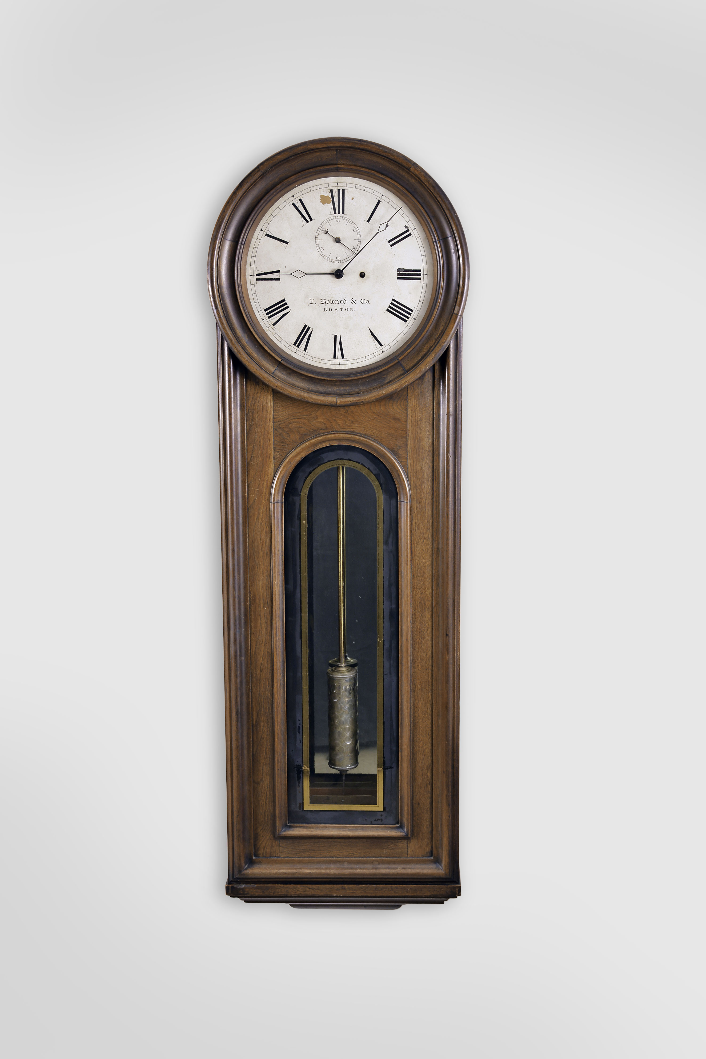 E. Howard & Co., Boston, Mass., "No. 12 Regulator", wall clock, 8 day, time only, weight driven movement with a meter long compensated mercury pendulum with glass jar, in a walnut case with a painted metal dial and reverse painted tablet and on a purpose made special order base from the factory that allows the clock to stand on the floor. — Antique Clocks Price Guide