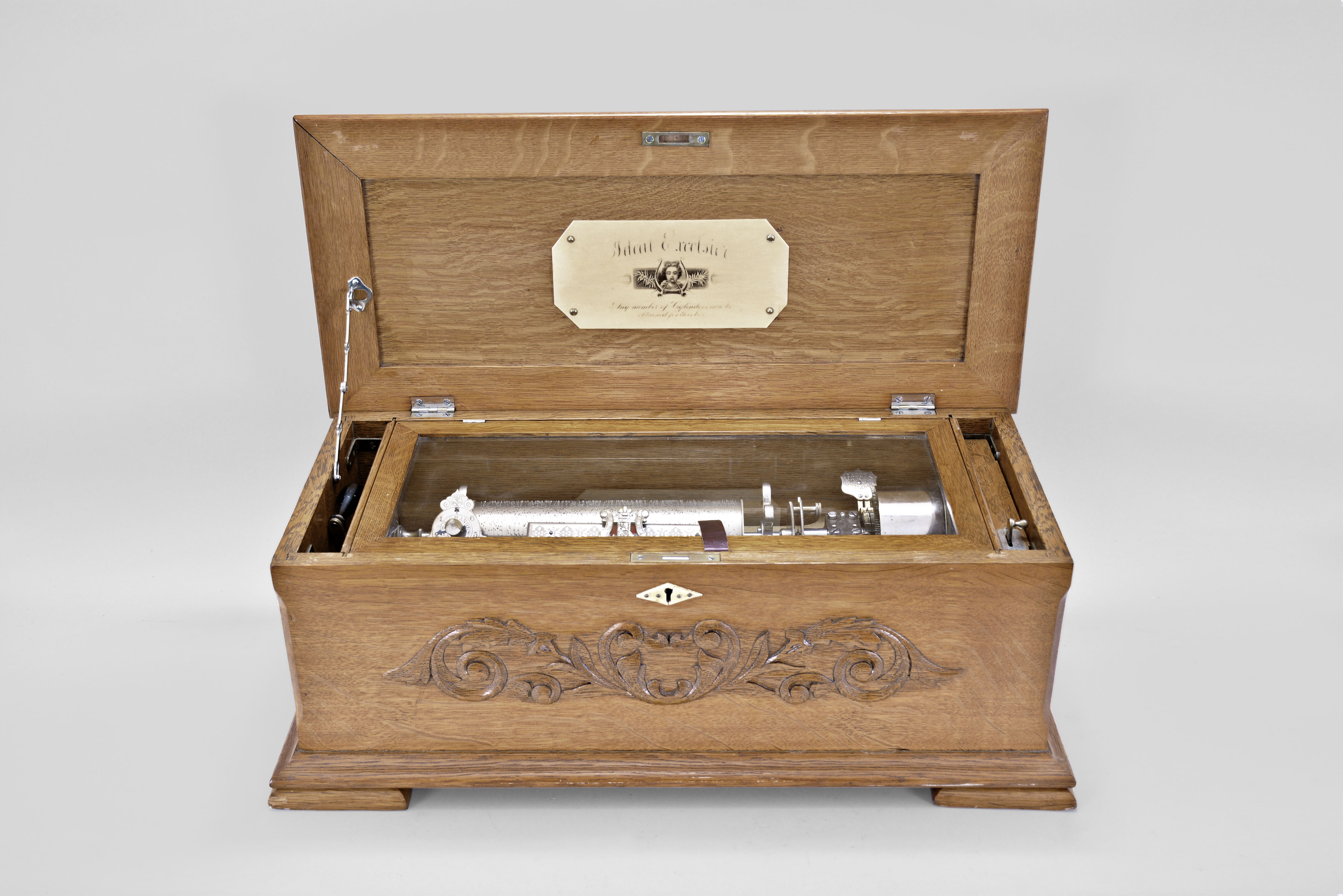 Switzerland for Heeren Bros. and Co., Pittsburgh, Penn., "Ideal Excelsior" interchangeable cylinder music box, 6 tunes using a 9 inch cylinder playing on a one piece comb with 60 teeth, mechanism with Jacot's safety check and speed control in a lidded oak case with molded base and top, applied oak ornament on the front, and retailer label under lid. The lot comes with four 9 inch cylinders which come in a matching oak case. — Antique Clocks Price Guide
