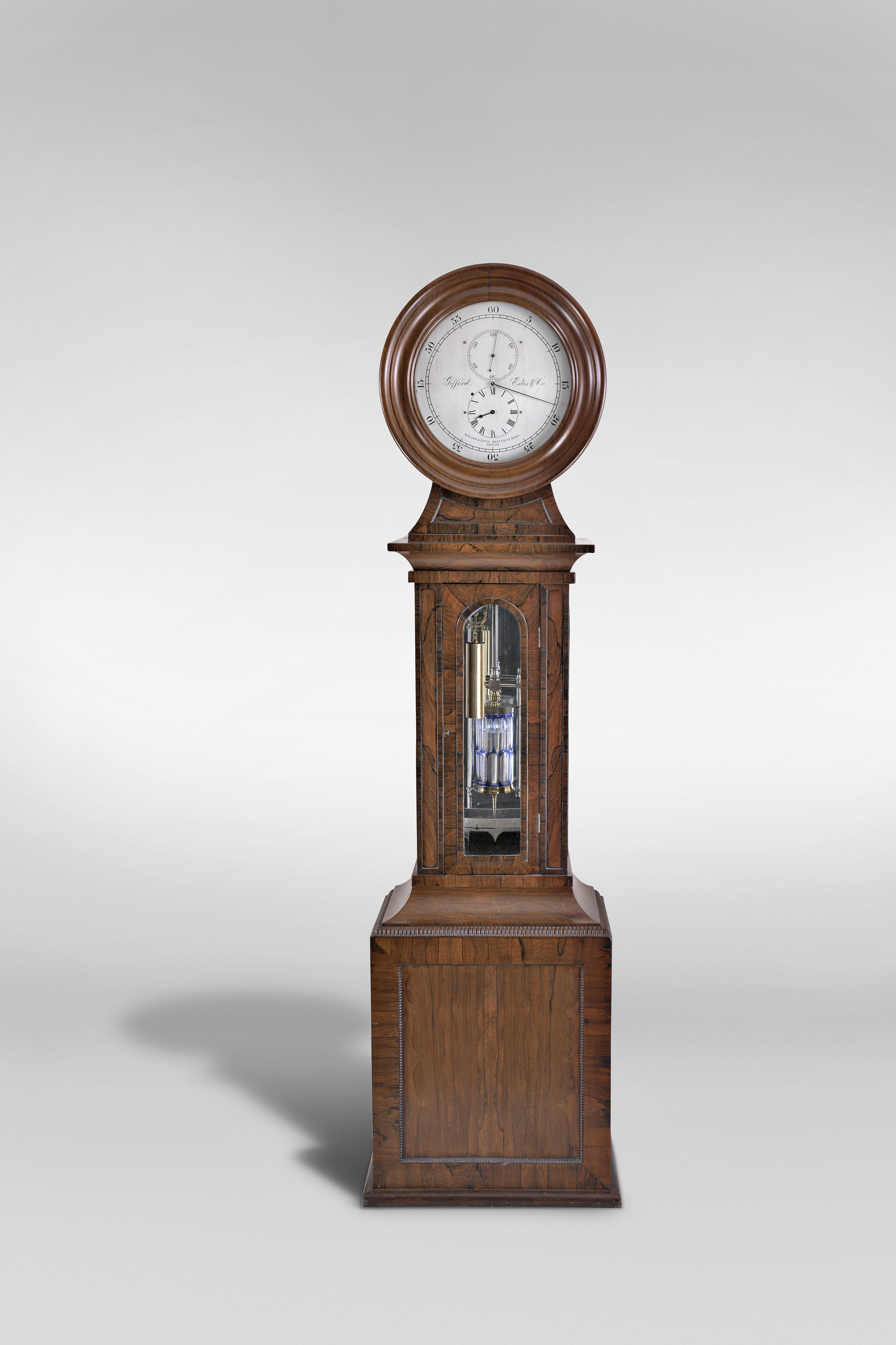 Howard & Davis, Boston, Mass., a rare astronomical standing regulator, walnut, rosewood and rosewood veneer drumhead case, the base with turned, quarter round bead moldings framing recessed panels at the front and sides, and finished with a deep cavetto molding transitioning to the trunk, the trunk door with arched, crossbanded opening for viewing the weight and pendulum, and flanked by two narrow faux panels with crossbanded surround, the case sides also with glazed, arched windows, and surmounted by a cavetto molding below an incurved transition piece with conforming, molded panel, and supporting the drumhead with turned, molded door before the silvered brass dial, signed "Gifford, Estes & Co.", and "Howard & Davis Manufacturers, Boston", blued steel hands, large 8 day, weight driven timepiece movement with brass counterpoise for minute hand, jewelled pallets, pallet arbor, and escape wheel, and having adjustable steel endpieces throughout, brass weight with lyre form pulley, mercury pendulum with steel rod and decorative steel components, and blue cased glass jar with elongated, oblong clear cut panels, and with silvered beat scale, all before a mirrored case back, catching and reflecting light, and enhancing the decorative aspects of the various components — Antique Clocks Price Guide