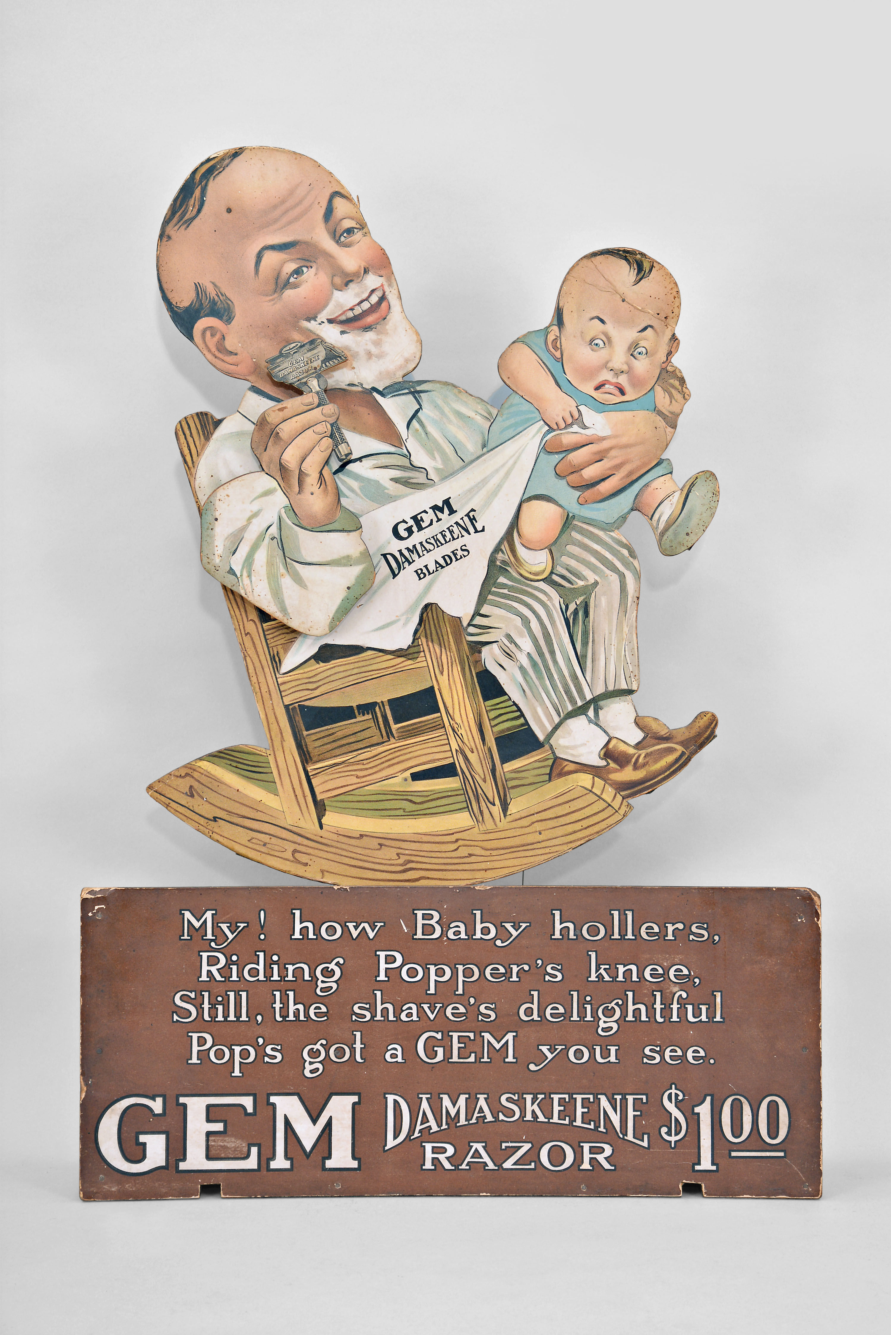 The Gem Cutlery Company, New York, "GEM Damaskeene Razor" animated advertising display, articulated pressboard figure of a father shaving with a baby on his knee, spring driven pendulum movement with simple escapement on a wood base. — Antique Clocks Price Guide