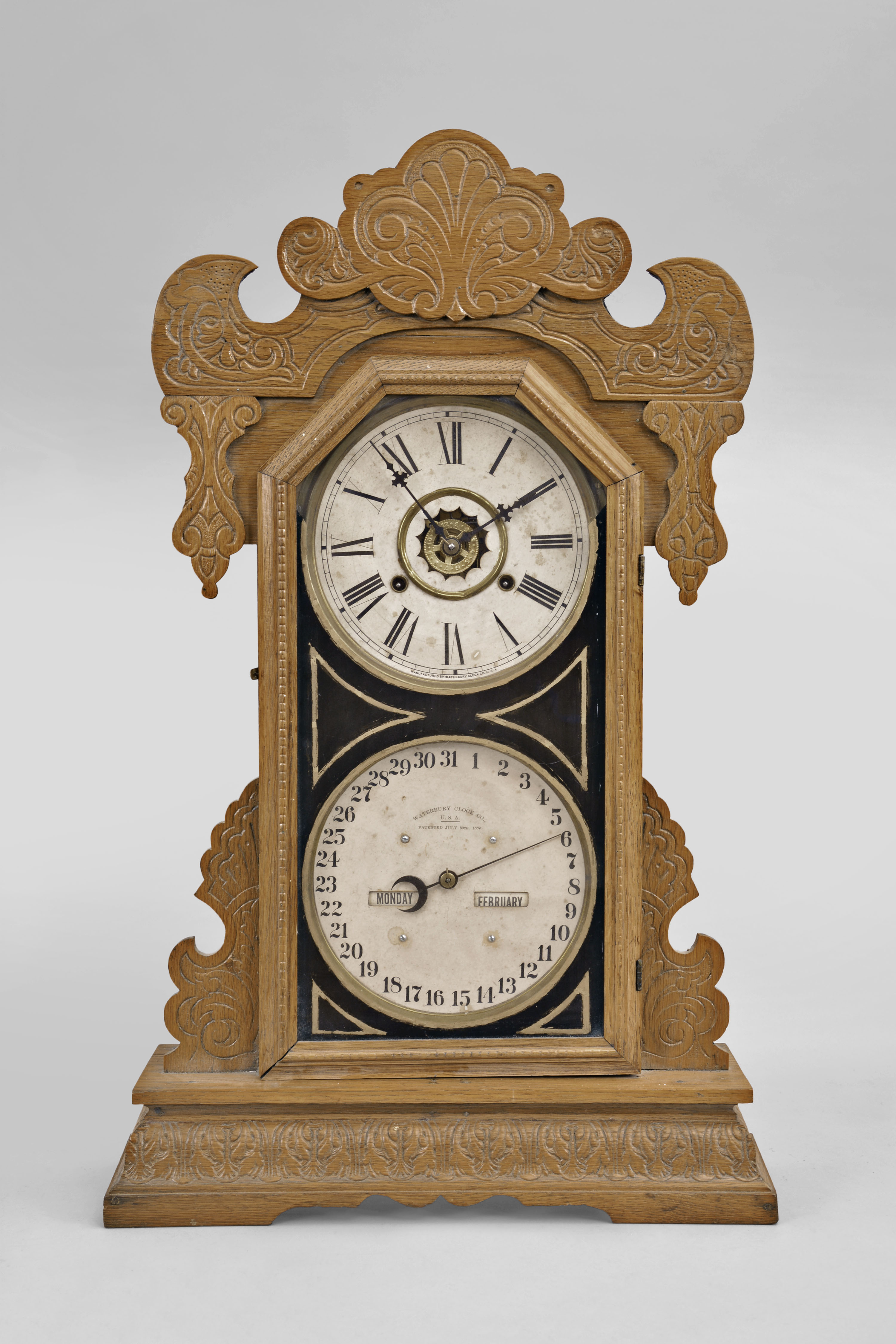 Waterbury Clock Co., Waterbury, Conn., "Oswego" double dial gingerbread style calendar clock, 8 day, time and strike with alarm and perpetual calendar, spring driven movement in an oak case. — Antique Clocks Price Guide