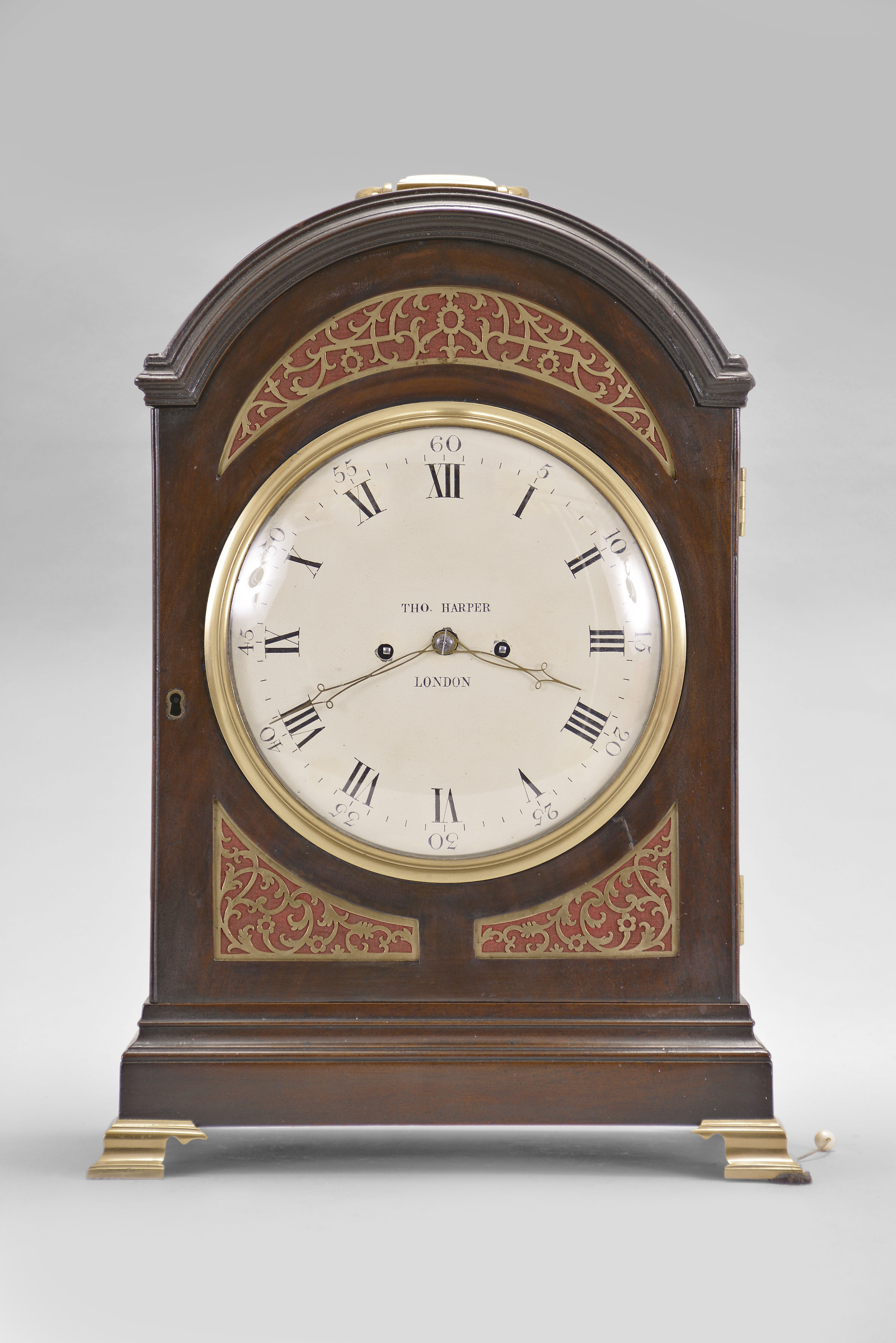 Thomas Harper, London, an 18th century mahogany bracket clock, the case with molded arch top and base, and on brass bracket feet, the case front with three textile backed brass frets, the upper crescent shaped, and the two lower frets conforming to the shape of the dial and case, the sides also with pierced frets, Roman numeral white painted dial with Arabic minutes, finely finished brass hands, two train fusee movement with verge escapement, the back plate with symmetrical foliate engraving and basket of flowers, the upper right corner stamped "2978", counting the hours on a bell, and repeating the last hour on demand — Antique Clocks Price Guide