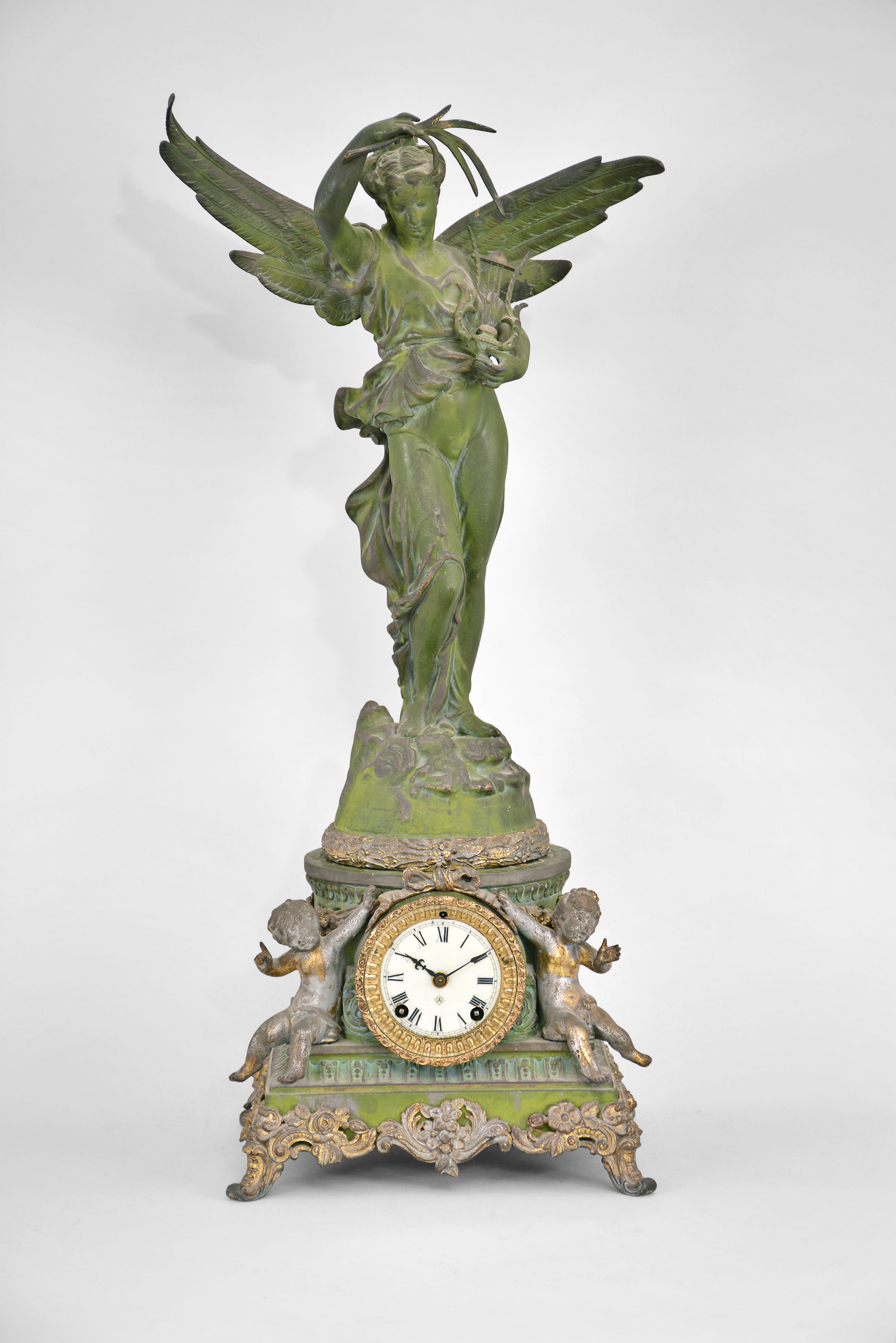 Ansonia Clock Co., New York, "Sibyl and Gloria" mantel clock, 8 day, time and strike, spring driven movement in a two-piece case featuring two putti flanking the white porcelain dial in the center of the base, the top with a large winged female figure holding a lyre. — Antique Clocks Price Guide