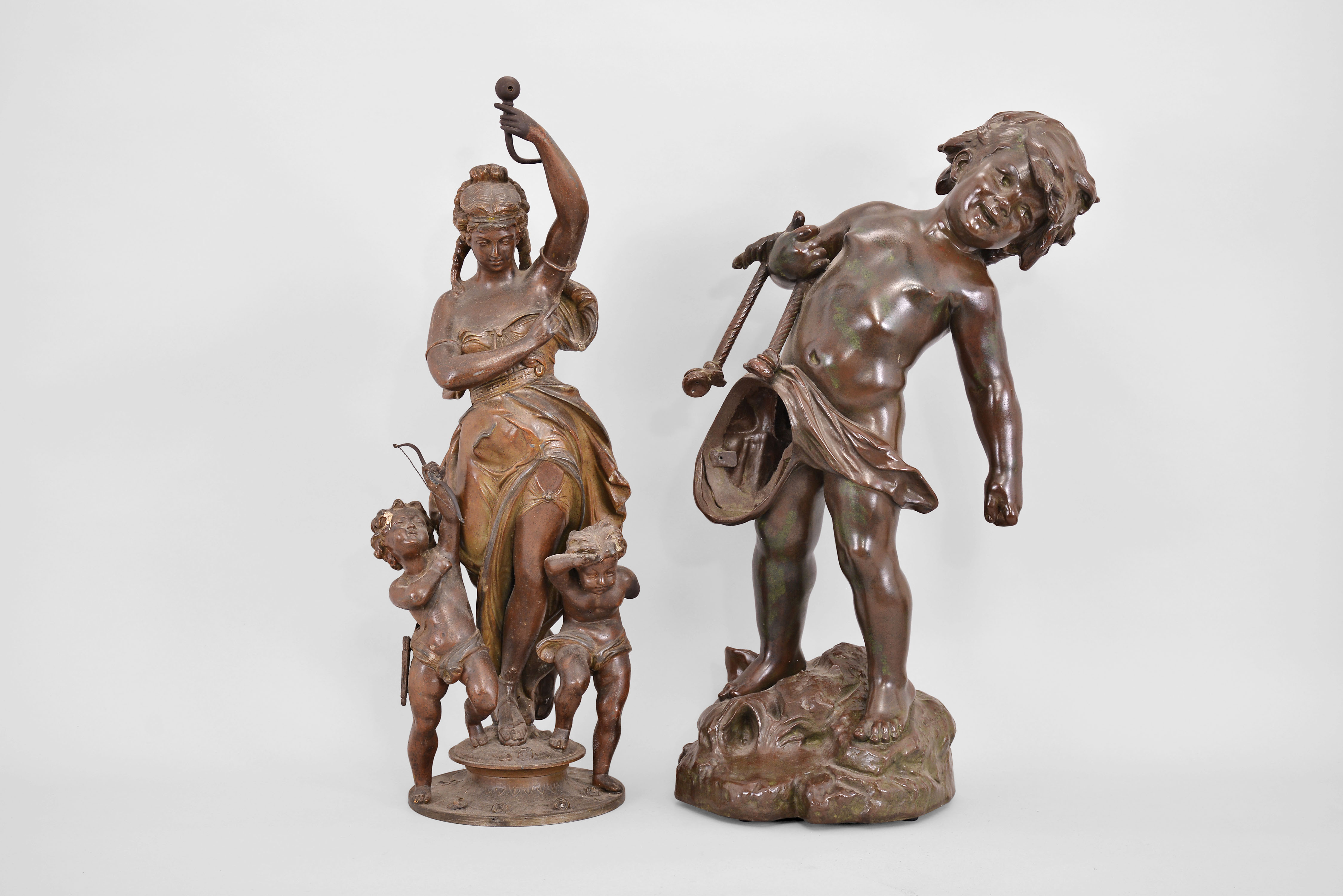 Parts- 2 (Two) Figural Statues: (1) France, after Auguste Moreau, "The Water Carrier", cast spelter with bronze patination, depicting a child carrying a large vase by a rope; (2) France, swinging mystery clock base, cast spelter with bronze patination, featuring a woman in flowing dress with two putti at her side, both early 20th Century. — Antique Clocks Price Guide