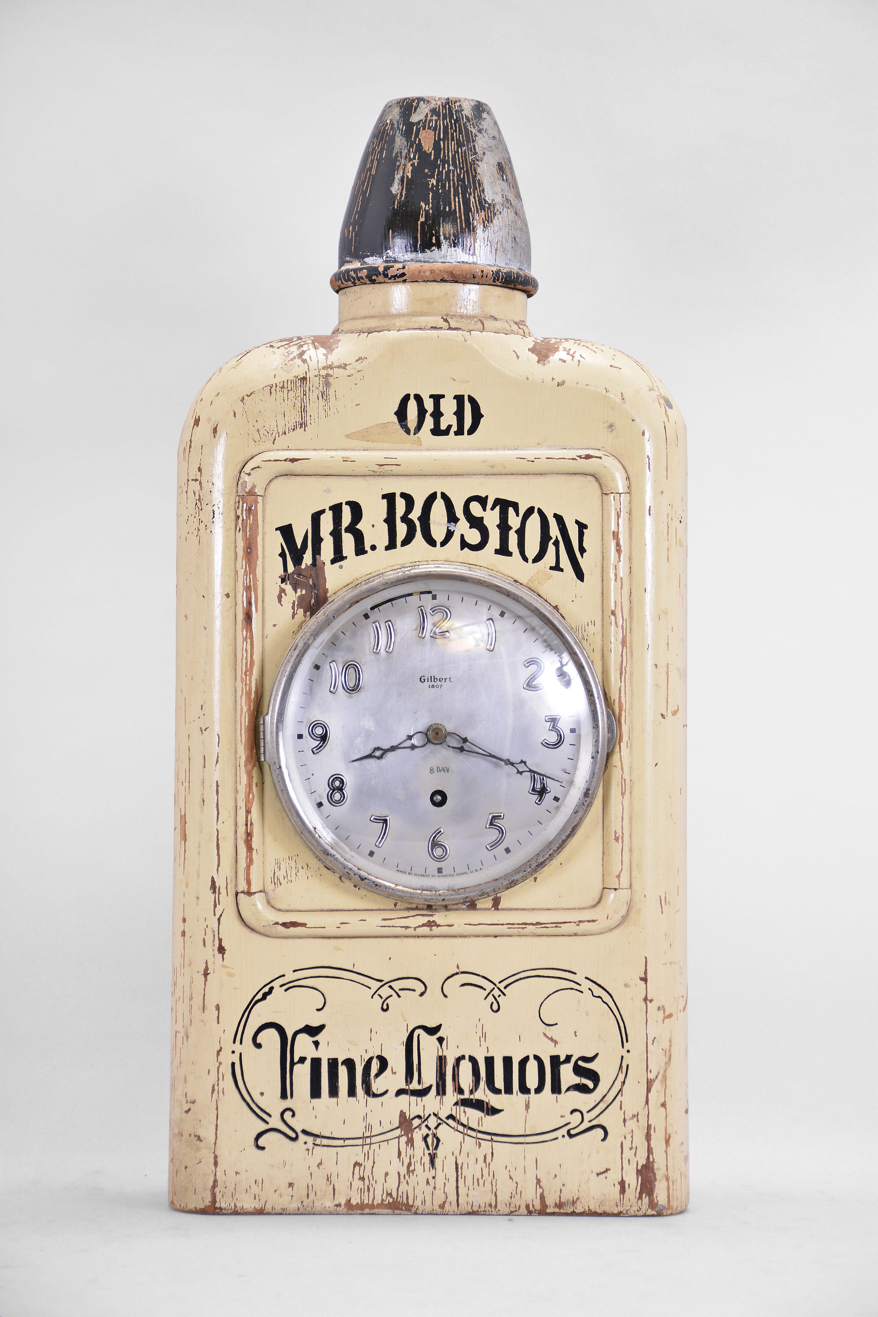 Wm. L. Gilbert Clock Co., Winsted, Conn., "Old Mr. Boston" novelty advertising clock, 8 day, time only, spring driven balance wheel movement in a solid wood case shaped and painted to look like a bottle of whisky, silvered dial and steel hands. — Antique Clocks Price Guide