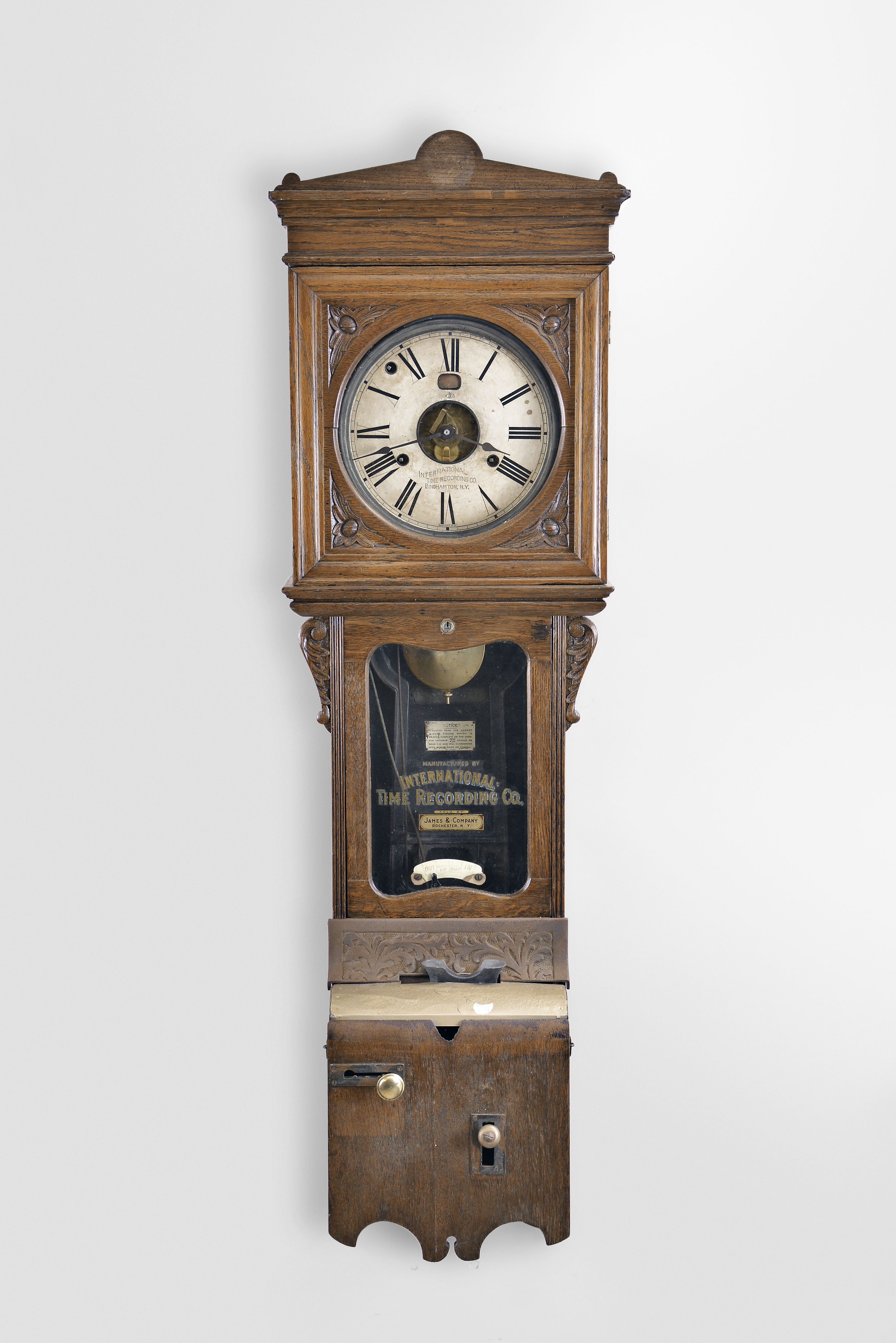 International Time Recording Co., Endicott, NY sold by James & Co., Rochester N.Y., wall hanging punch clock, 8 day, time and day of the week, spring driven movement in an oak case with punch mechanism and painted metal dial with exposed center and day of the week aperture — Antique Clocks Price Guide