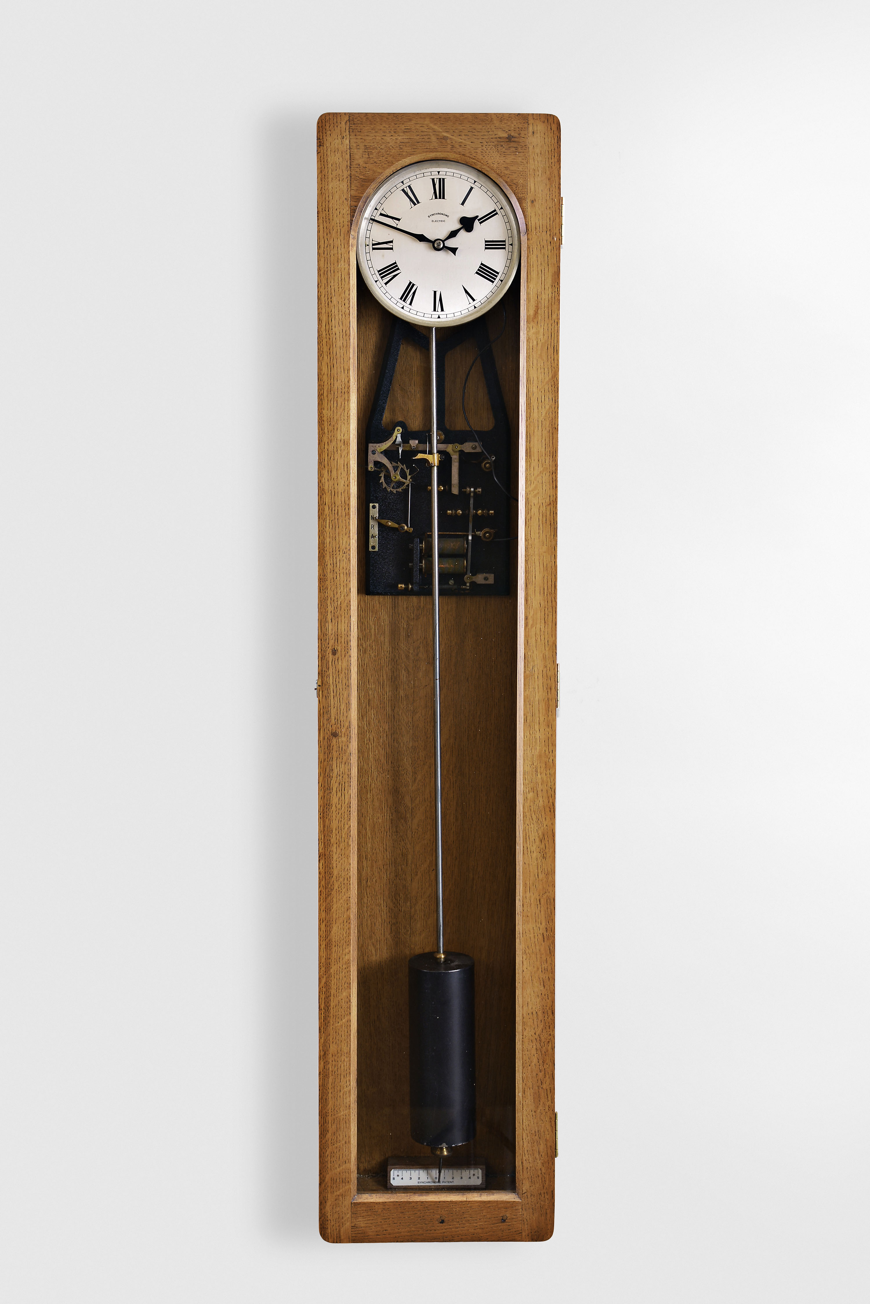 The Synchronome Co., Ltd., England, master clock, oak case, Roman numeral silvered dial, electromechanical movement providing impulse every thirty seconds from a falling gravity arm to pendulum and cylindrical bob, NRA #3439 — Antique Clocks Price Guide