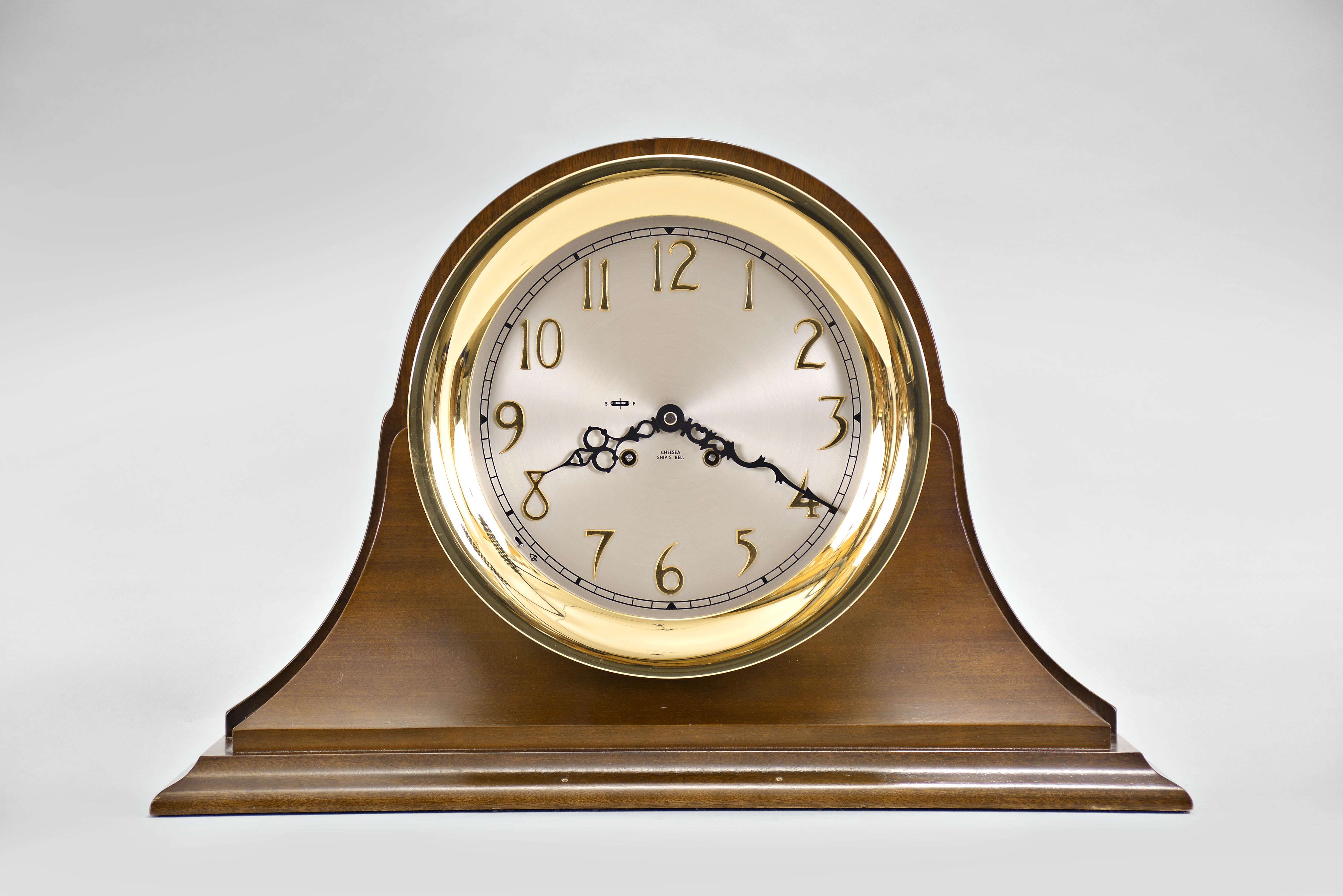 Chelsea Clock Co., Boston, Mass., "Ship's Strike" shelf clock, 8 day, time and ship's bell strike, spring driven movement in a round brass case with silvered metal 10 inch special dial with applied brass numerals set on a mahogany base — Antique Clocks Price Guide