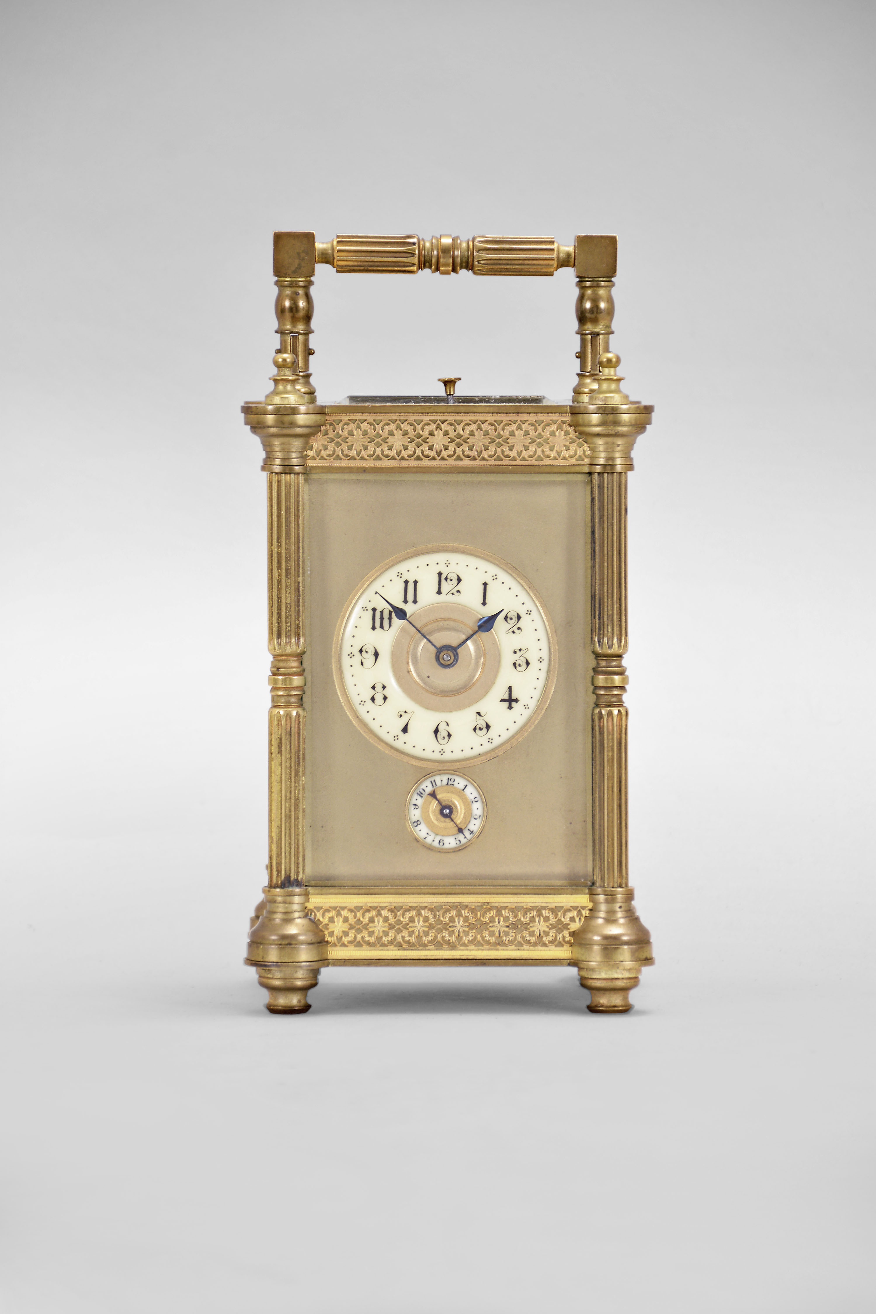 France, Pillars variant hour repeating carriage clock, the glazed, gilt brass case with turned feet, fluted columns, and turned finials, the base and frieze with gilt, blind fret, and the case top with carrying handle matching the columns, gilt dial mask enframing the Arabic numeral white enamel dial, with subsidiary enamel alarm dial below 6:00, blued steel spade hands, 8 day, three train movement with lever platform, striking the hour and half hour in passing, and repeating the last hour on demand, and with H.B. mark within an upturned crescent — Antique Clocks Price Guide