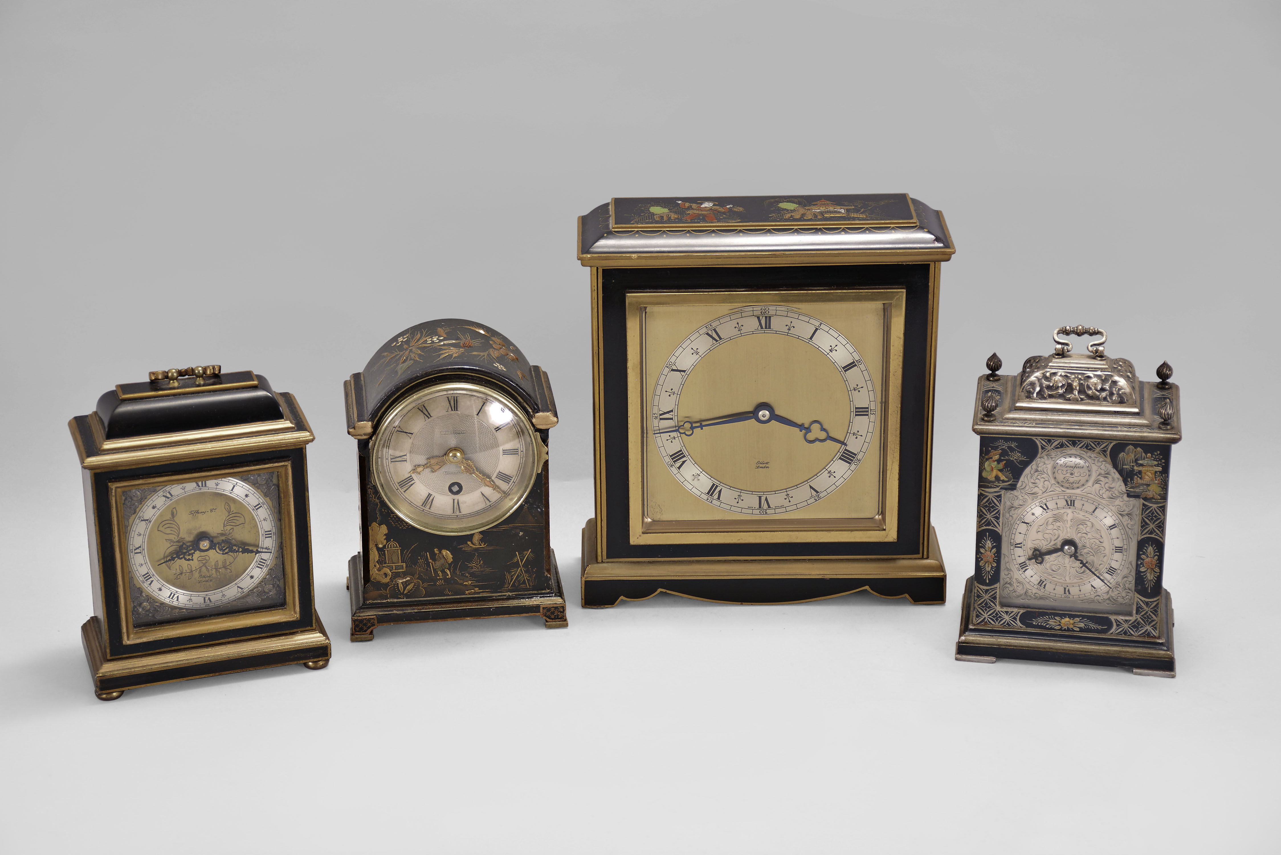 Clocks- 4 (Four) Japanned desk clocks, 8 day, time only, spring driven movements: (1) Elliott, London, desk clock with a square case with molded top and base; (2) Elliott, London, miniature bracket clock, black case with gold trim; (3) Samuel Marti for J.E. Caldwell, Philadelphia, miniature bracket clock with guilloche silvered dial. (4) Canham, London, miniature bracket clock with engraved silvered dial. — Antique Clocks Price Guide