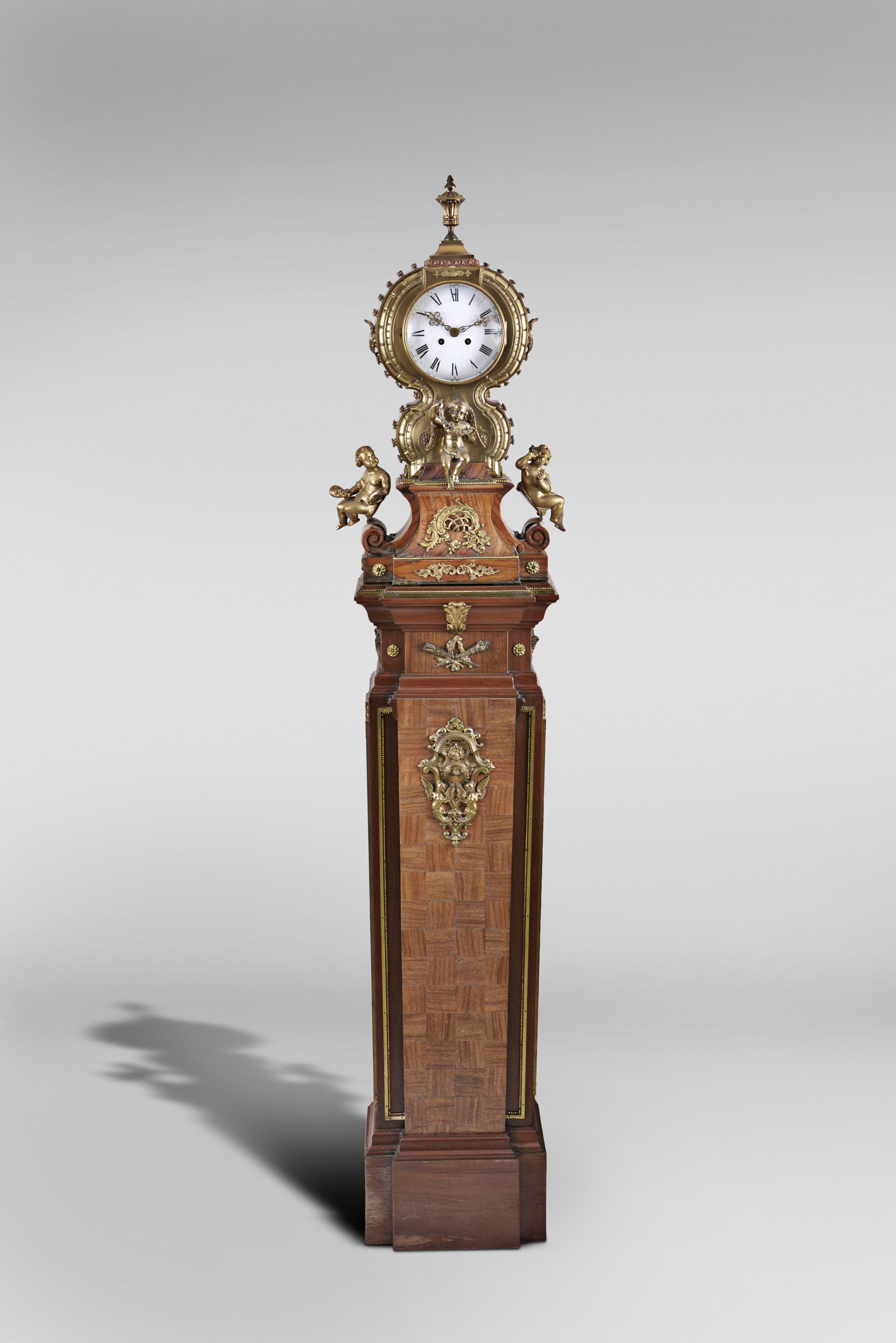 Marti & Cie, Paris, France, figural shelf clock, 8 day, time and strike, spring driven movement with white enamel dial in a highly stylized cast brass case set on veneered wooden base surmounted by three putti grasping bacchanal themed items and cast brass appliques including matching stand with cast brass appliques, veneers and ornaments. — Antique Clocks Price Guide