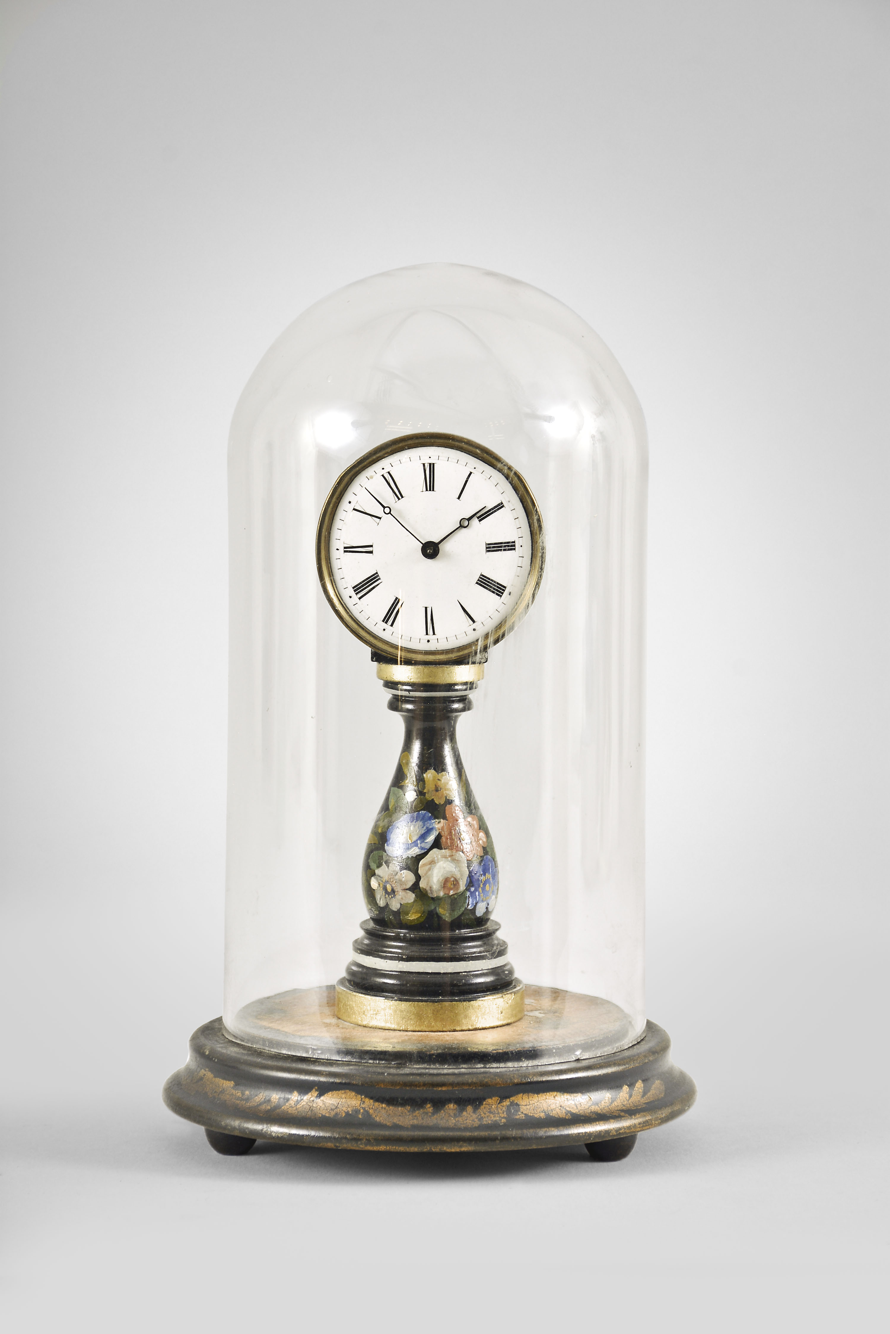 A small, European candlestand clock, ebonized baluster form base with floral decoration supporting a roman numeral white enamel dial with blued steel Breguet style hands, 30 hour timepiece movement with tic tac escapement, all mounted to a decorated turned wooden base with glass dome — Antique Clocks Price Guide