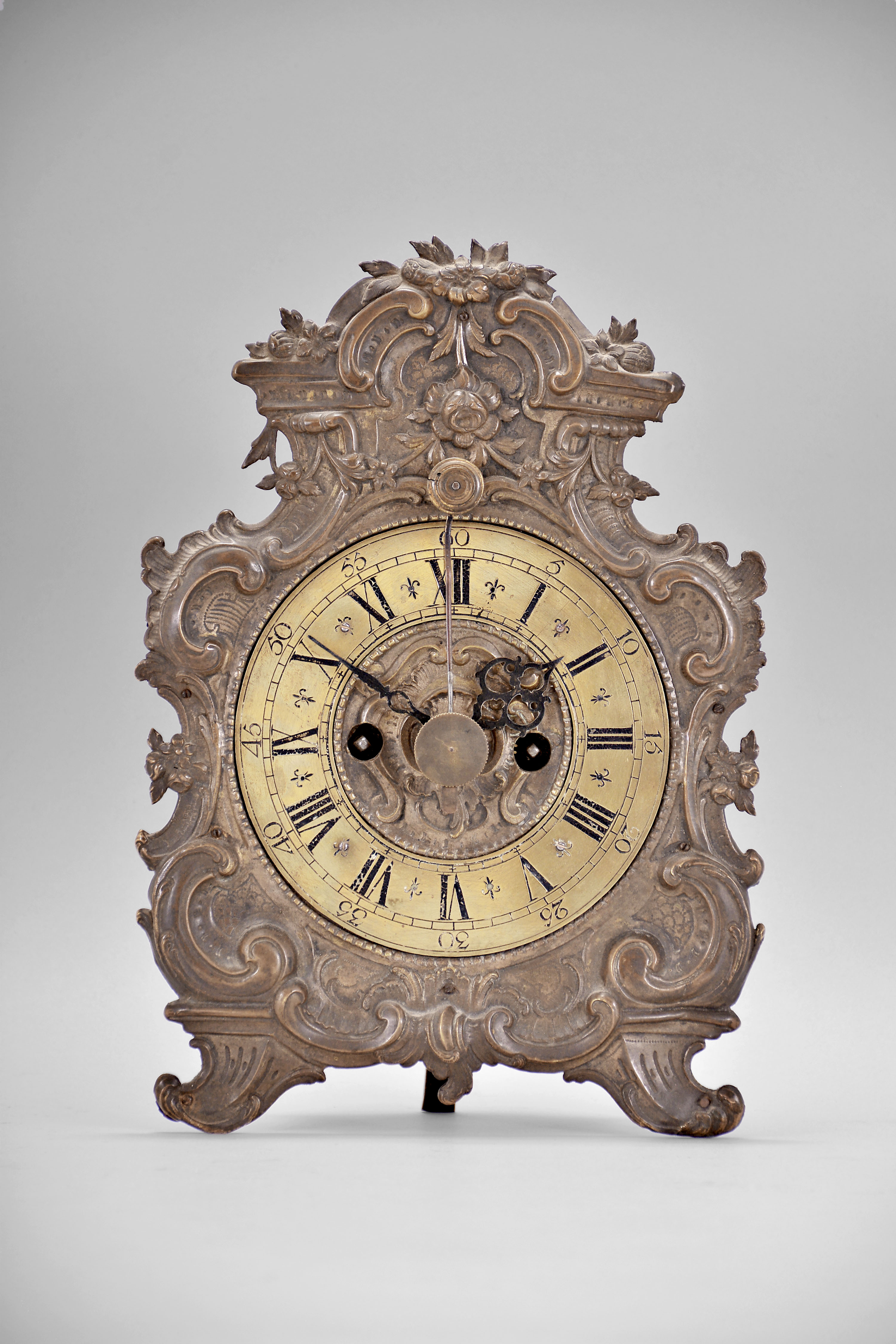 Germany, standing telleruhr, 8 day, time and strike, spring driven iron-plate movement with verge escapement and cowtail pendulum swinging in front of the dial, the movement mounted to iron plate faced with brass relief of scrolls and flowers, brass chapter ring with Roman numerals for the hours and Arabic numerals every 5 minutes, pierced brass hands. — Antique Clocks Price Guide