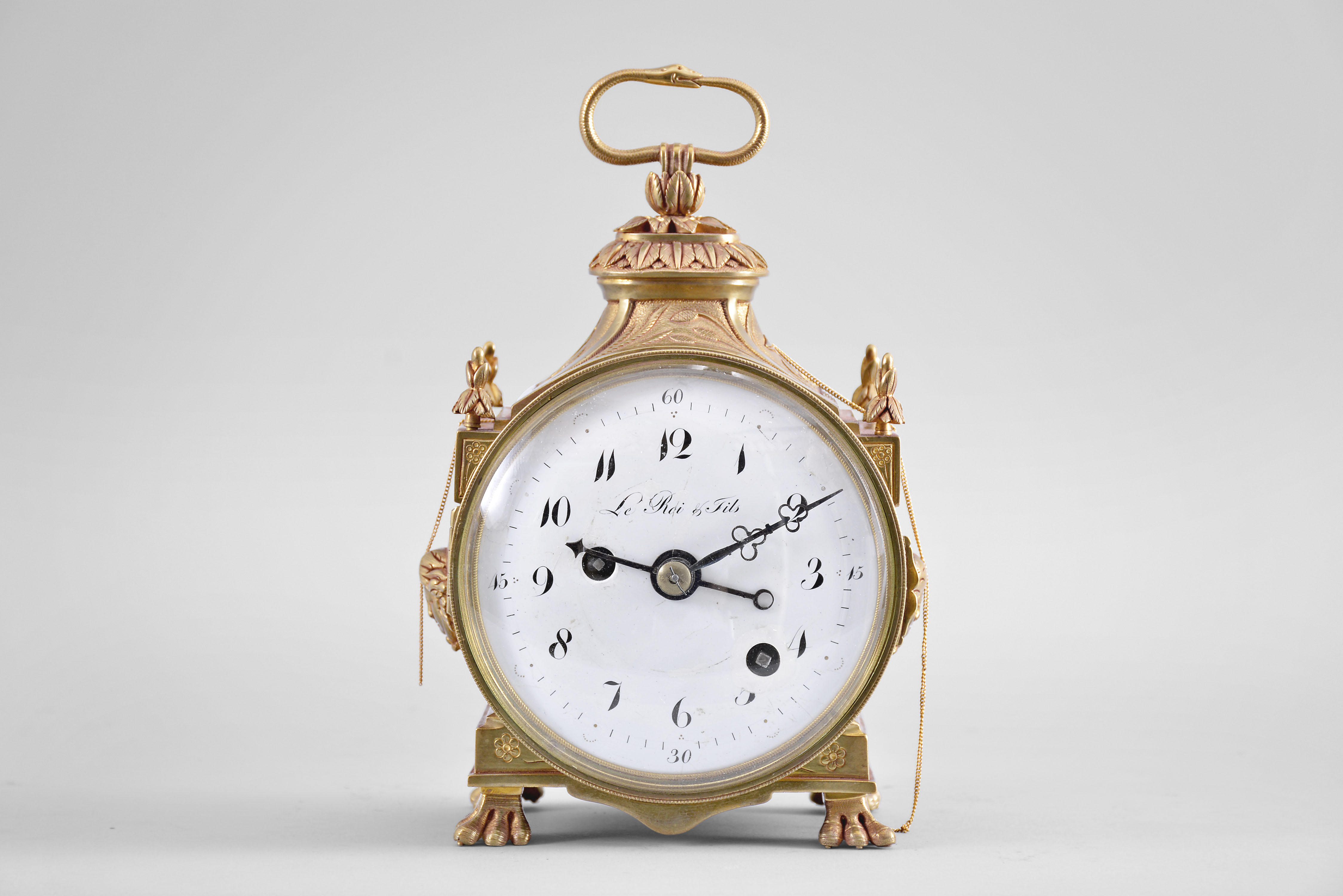 Le Roi & Fils, Paris, a late 18th century grand sonnerie striking Pendule d'Officier, the round gilt bronze case with stepped, rectangular base on paw feet, the sides with applied Medusa masks below a wheat ear ornamented frieze and foliate finials at the corners, and with incurved top, surmounted by an oval, foliate ornament with folding ouroboros handle, hinged brass bezel with convex beveled glass, Arabic numeral white enamel dial, blued steel hands, 30 hour, grand sonnerie striking and repeating movement with alarm, time train with fusee, strike train with barrel, the alarm wound by pulling a fine chain at the left side of the case, the repeating activated through a chain at the right, strike work mounted to back plate, and with verge escapement, the plain three arm balance visible beneath the pierced balance bridge, mounted to the back plate, the back plate stamped "SRF " — Antique Clocks Price Guide