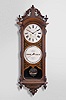 Ithaca Calendar Clock Co., Ithaca, New York, "No. 0 Bank", wall clock, 8 day weight driven movement with perpetual calendar, in a walnut case with a carved pediment top, carved base, ornately carved dial surround and upper and lower finials with papered metal dials