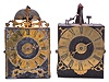 Clocks- 2 (Two) Early Comtoise: (1) France, Comtoise clock, 8 day, time and strike, weight driven movement with verge escapement, thread suspension with rear-hanging pendulum in a iron post and plate frame, brass chapter ring with engraved Roman numerals, applied spandrels and pivoted winding arbor shutters, single brass hand, topped by flat pierced brass fronton, first half of the 18th Century. (2) France, Comtoise clock, 8 day, time and strike with alarm, weight driven movement with verge escapement, thread suspension with rear-hanging pendulum in a iron post and plate frame, brass chapter ring with engraved Roman numerals, applied spandrels and pivoted winding arbor shutters, single brass hand, first half of the 18th Century.