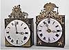 (1) France, Comtoise clock, 8 day, time and quarter strike, weight driven movement with verge escapement, thread suspension with rear-hanging pendulum in an iron post and plate frame, convex white enamel dial with Roman numerals for the hours, two pierced brass hands, cast bronze fronton featuring the sun and/or Apollo, flowers, and a sheaf of wheat, c1800; (2) France, month-running Comtoise clock, 30 day, time and strike with alarm, weight driven movement with verge escapement, thread suspension with front-hanging pendulum in a posted iron case, convex faience dial with Roman numerals for the hours, and Arabic numerals at the quarters, brass alarm ring with Arabic numerals, two brass hands, cast eagle spandrels, and cast fronton with central sun and eagle images, c1810.