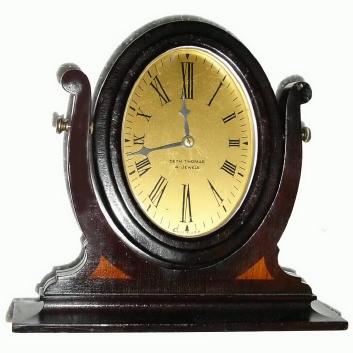 C.1930, Seth Thomas, desk clock, the movement and dial mounted in an oval mahogany frame, the whole setting in a yoke, accented with beechwood inlay. — Antique Clocks Price Guide